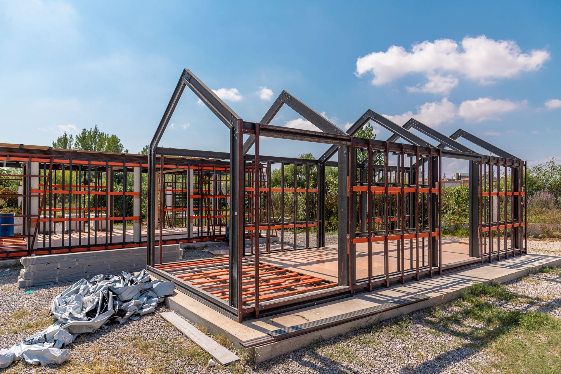 Steel-framed house under construction with exposed wooden trusses and red brick walls on a sunny day