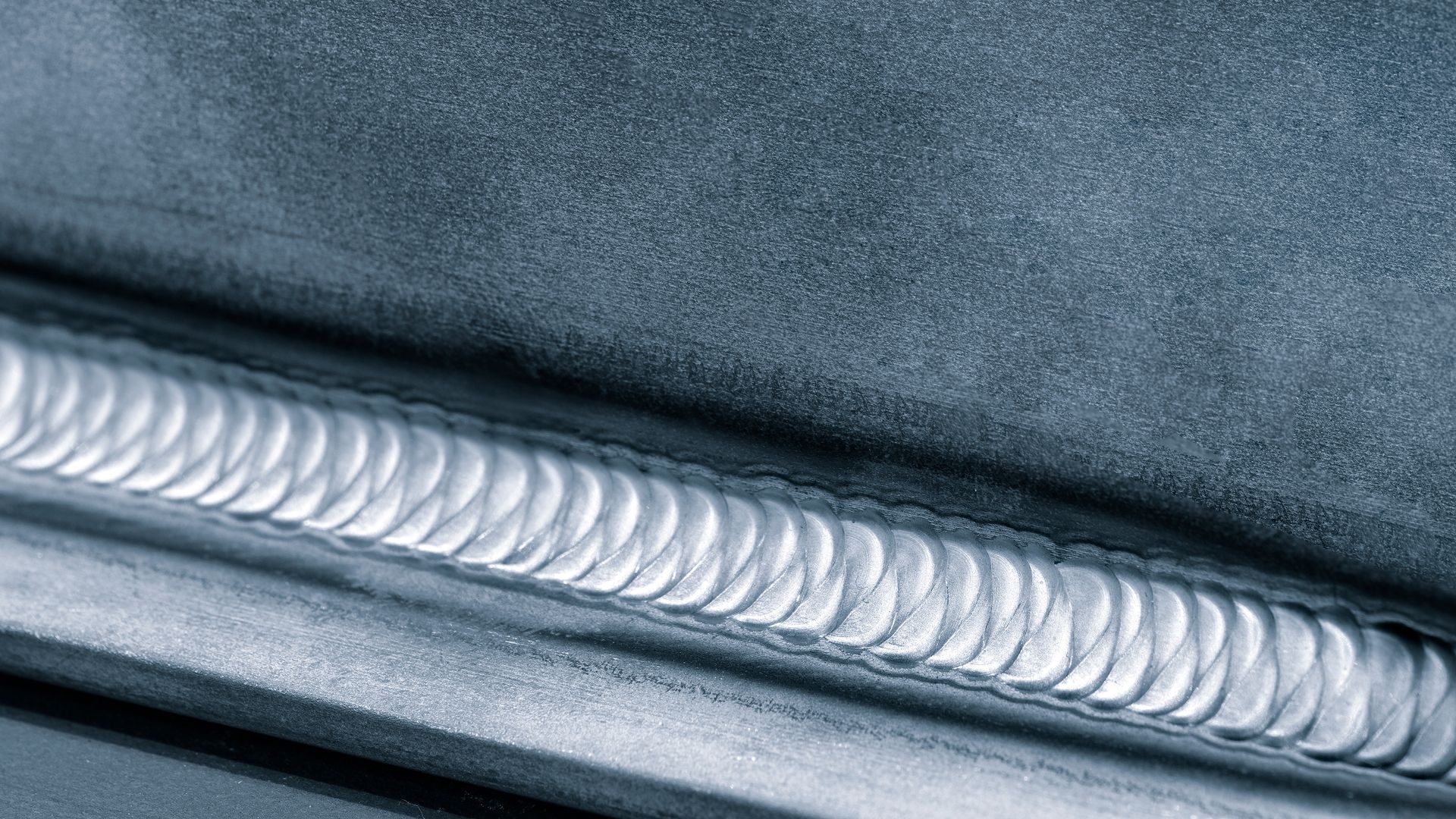 Close-up of a silver welded seam on dark fabric or metal surface