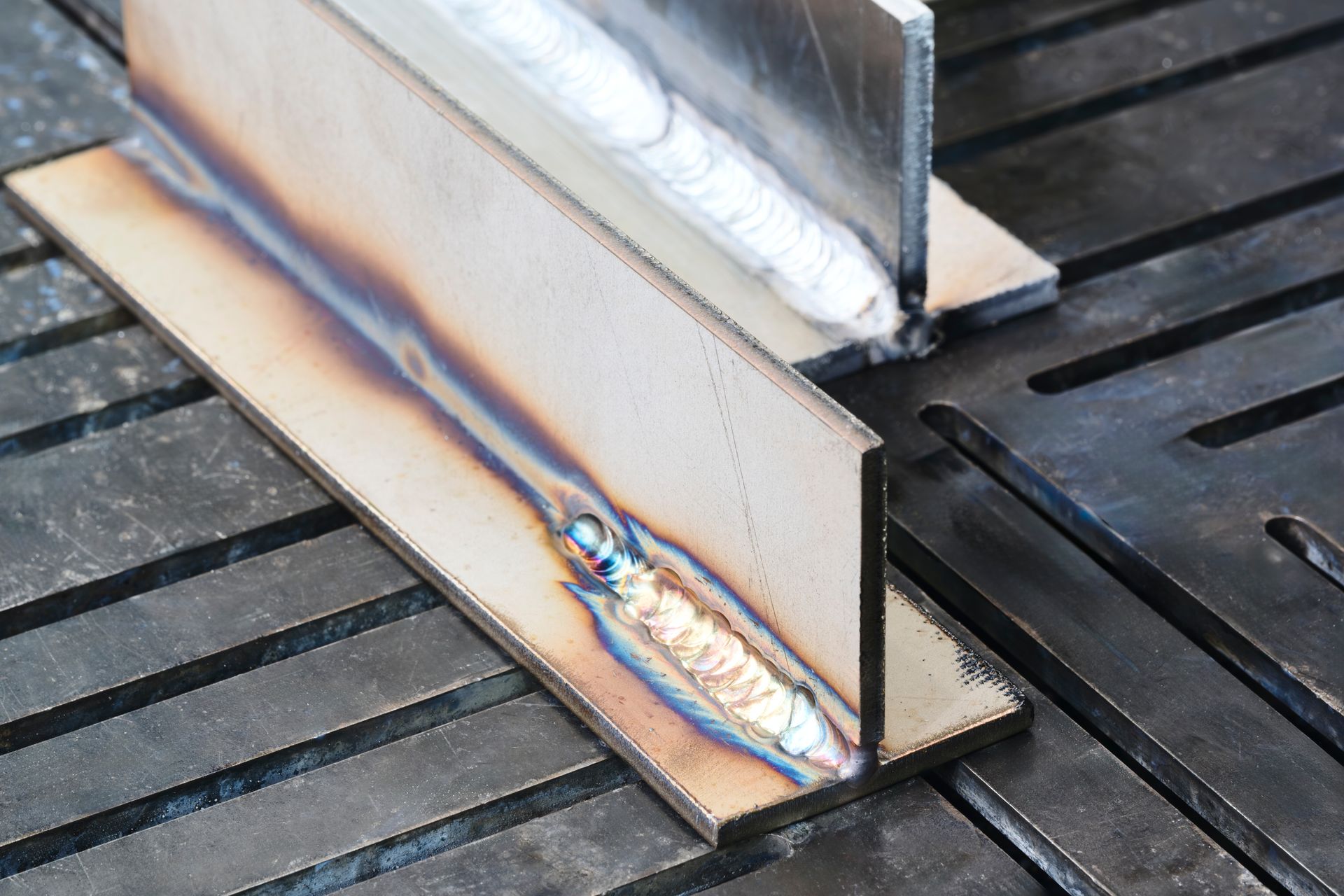 Two welded steel angle irons on a workbench, with visible weld beads and heat discoloration