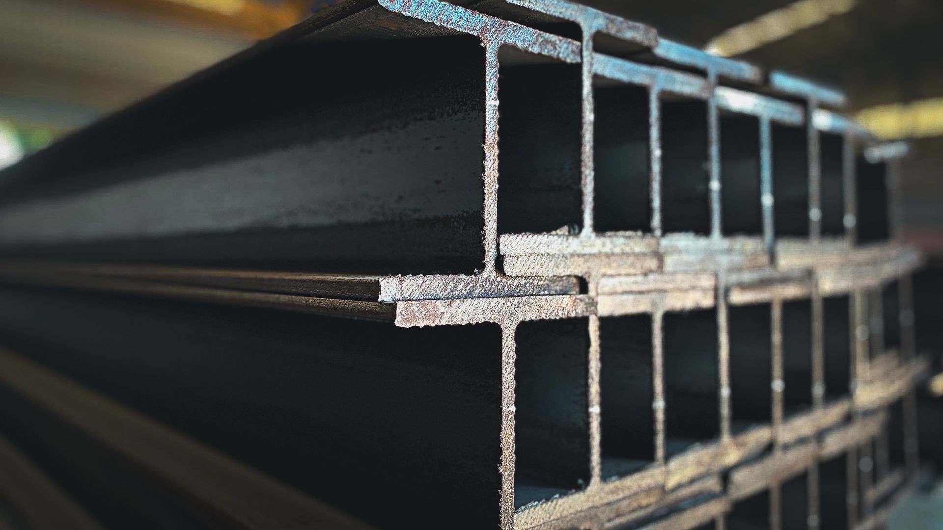 Stacked metal I-beams with hollow rectangular ends, shown in close-up at an industrial site.