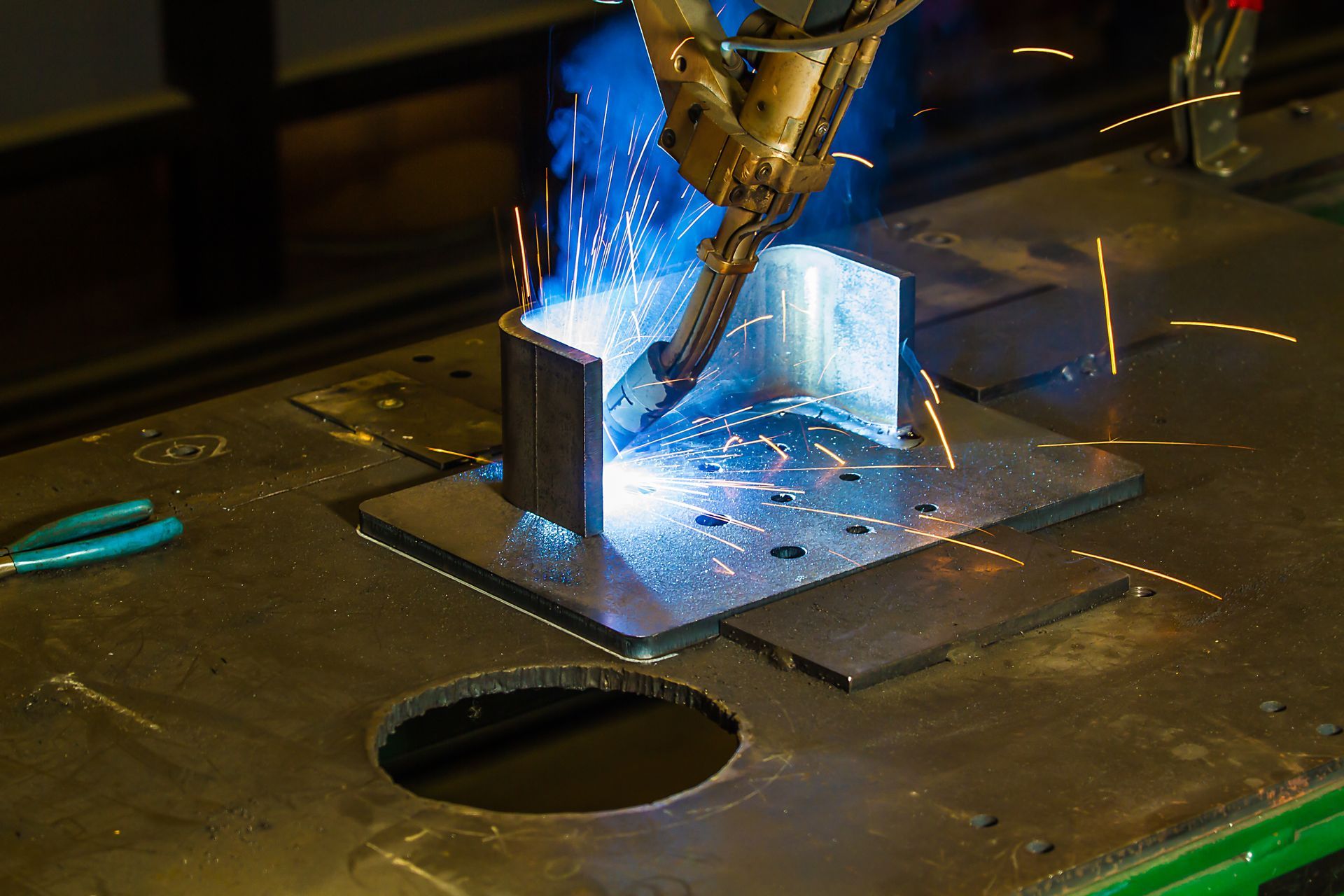 A welding torch cutting metal on a workbench, with bright blue sparks and glowing metal edges.