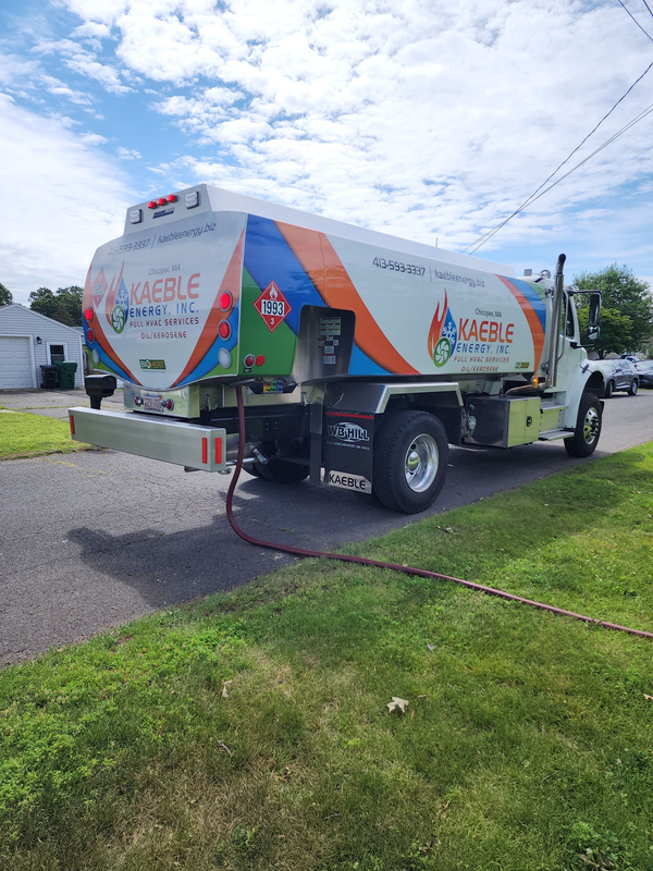 A man is walking towards a tanker truck with a hose attached to it.
