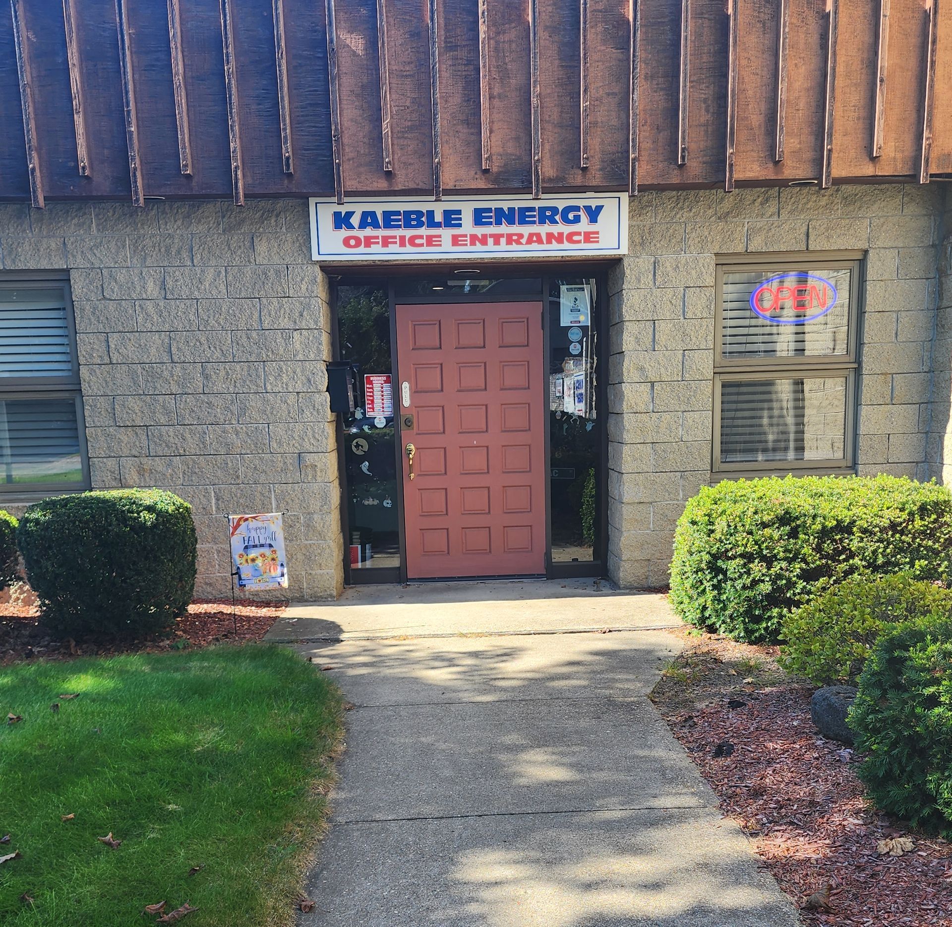Office entrance for Kable Energy; brown door, sign, brick building, bushes, and a sidewalk.