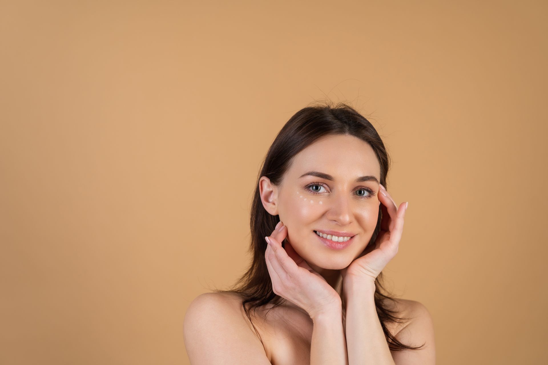 A woman is touching her face with her hands and smiling.