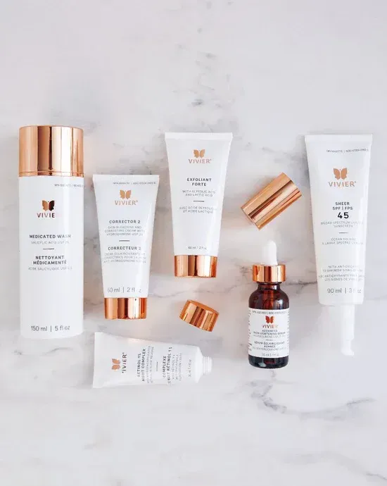 Skincare products: white bottles with gold caps arranged on marble surface.