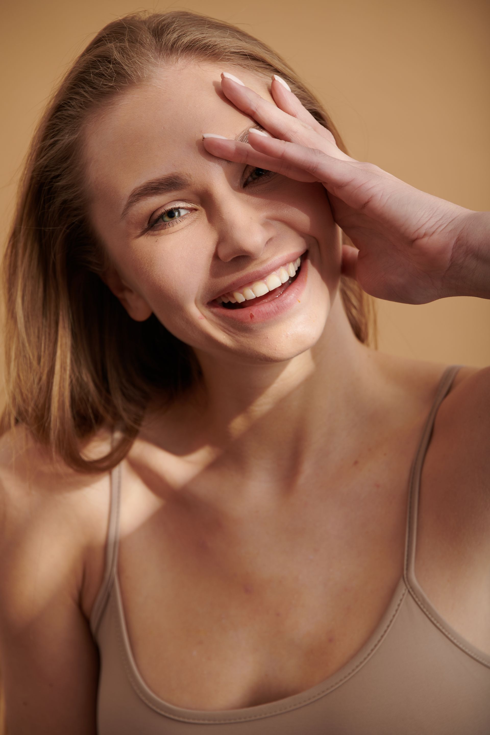A woman in a tank top is smiling and covering her face with her hand.
