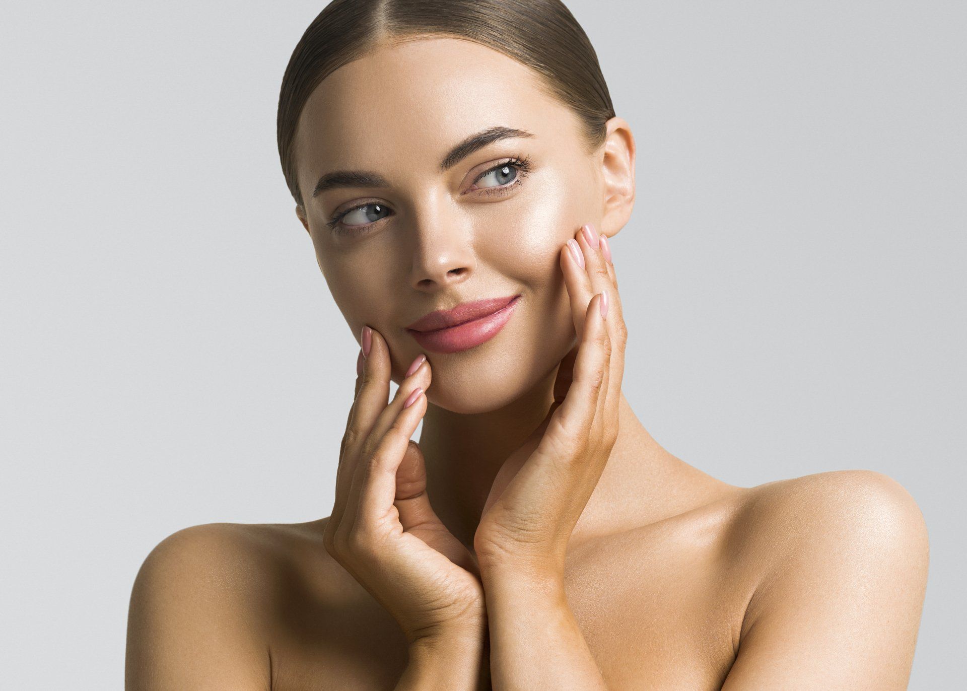 A woman is touching her face with her hands and smiling.