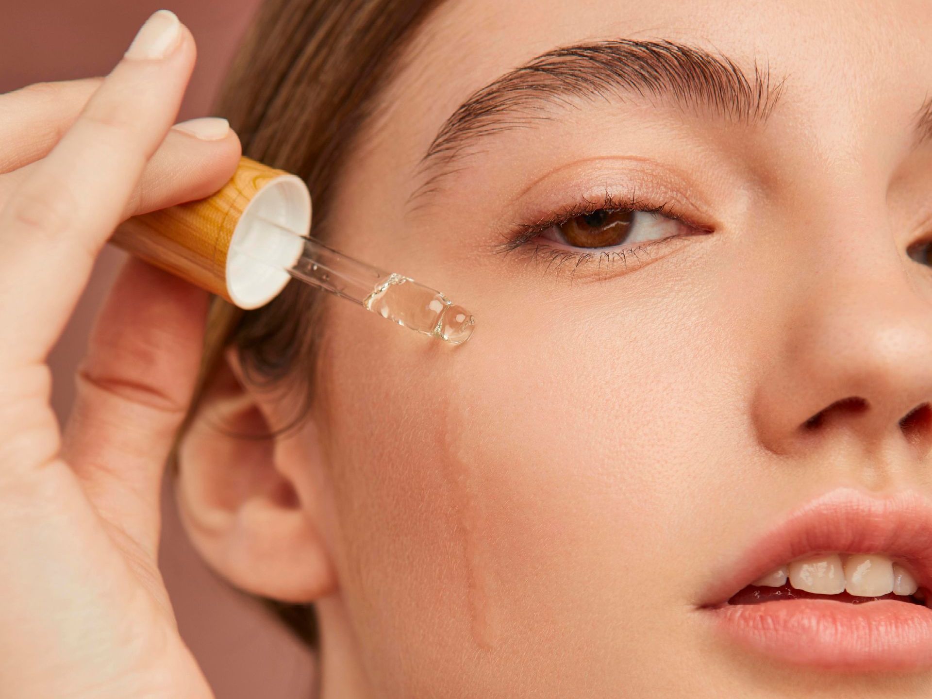 A woman is applying a serum to her face with a pipette.