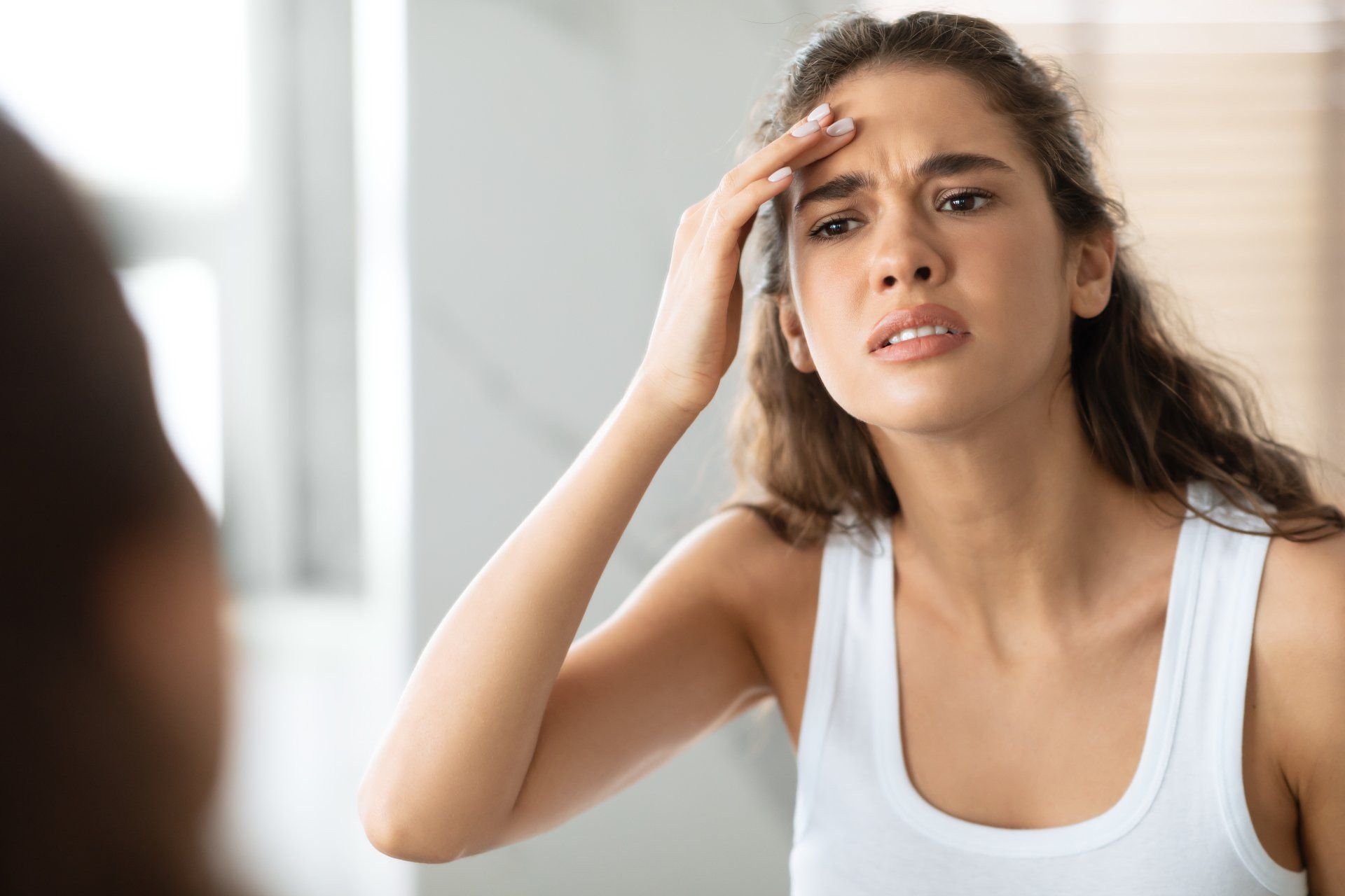 A woman is looking at her face in the mirror.