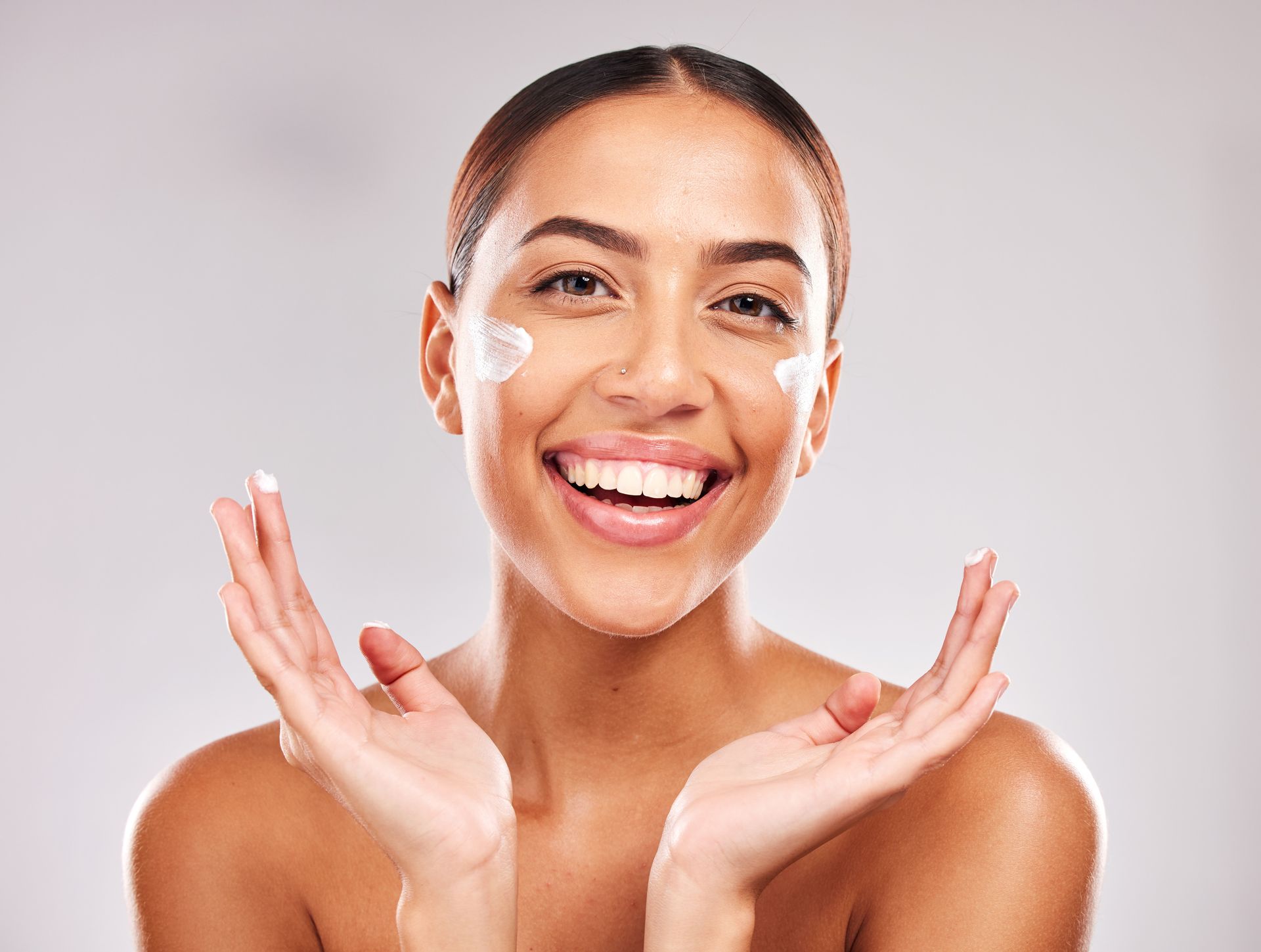 A woman is smiling while applying cream to her face.