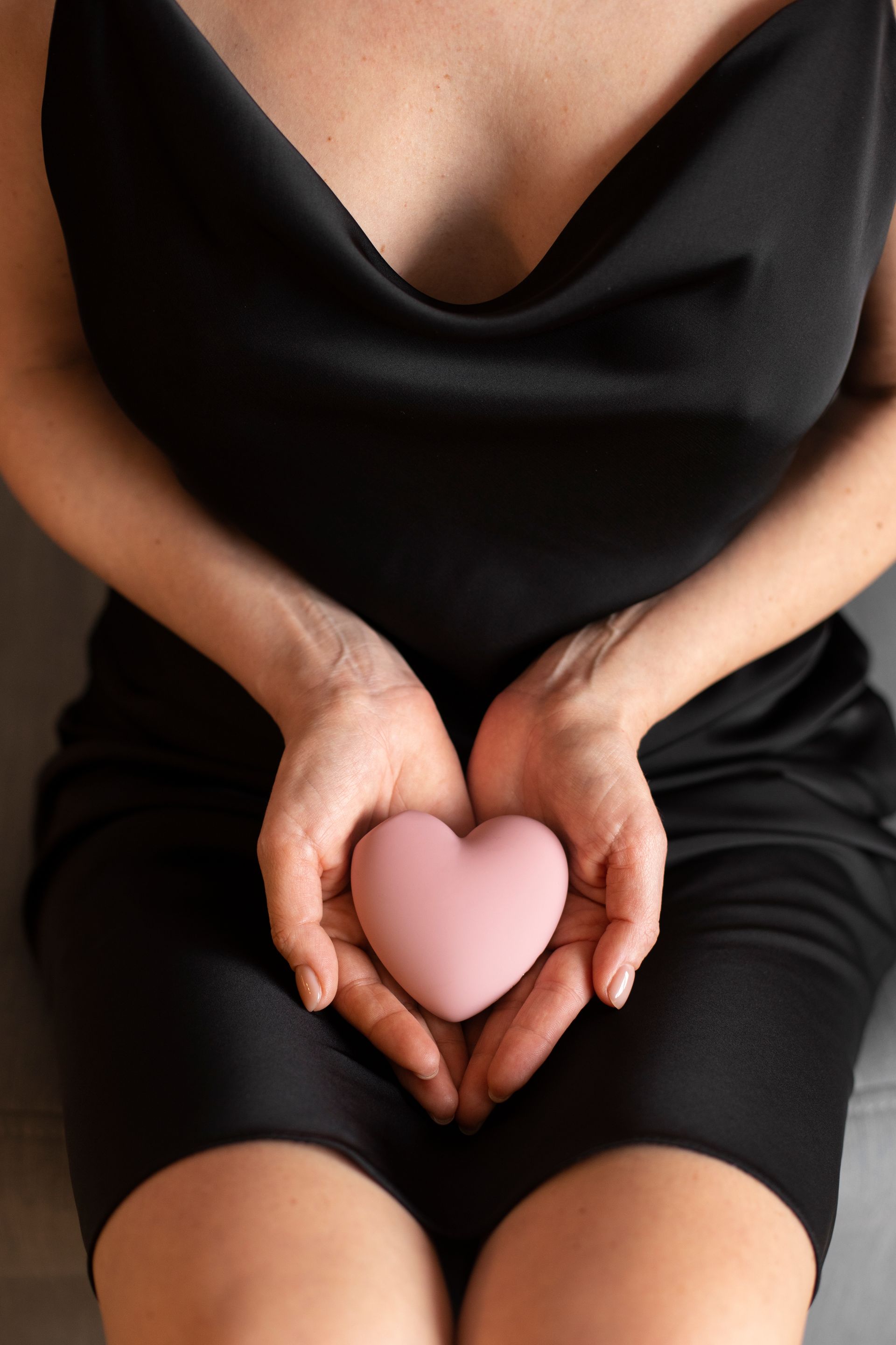 A woman in a black dress is holding a pink heart in her hands.