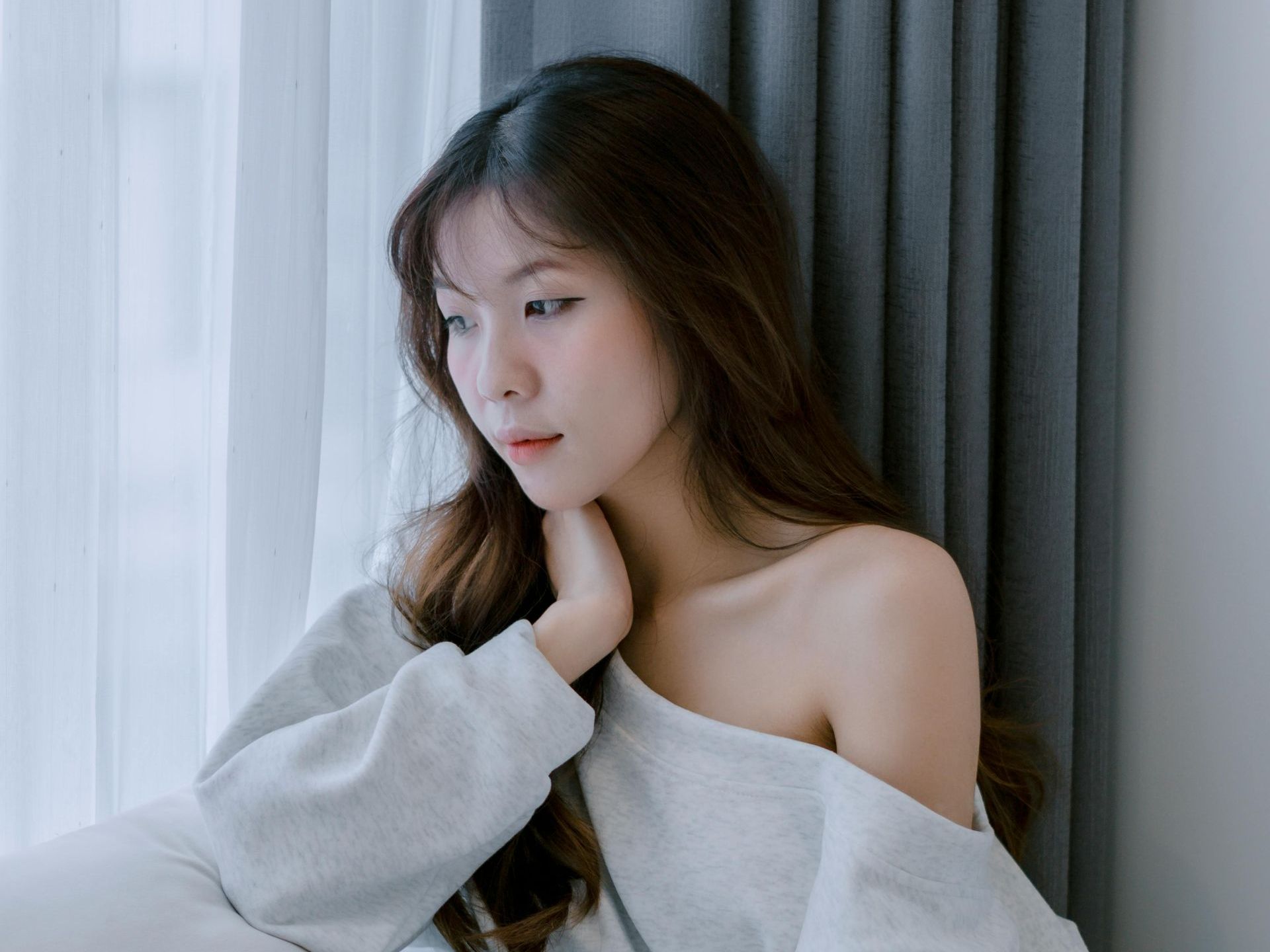 A woman is sitting in front of a window looking out.
