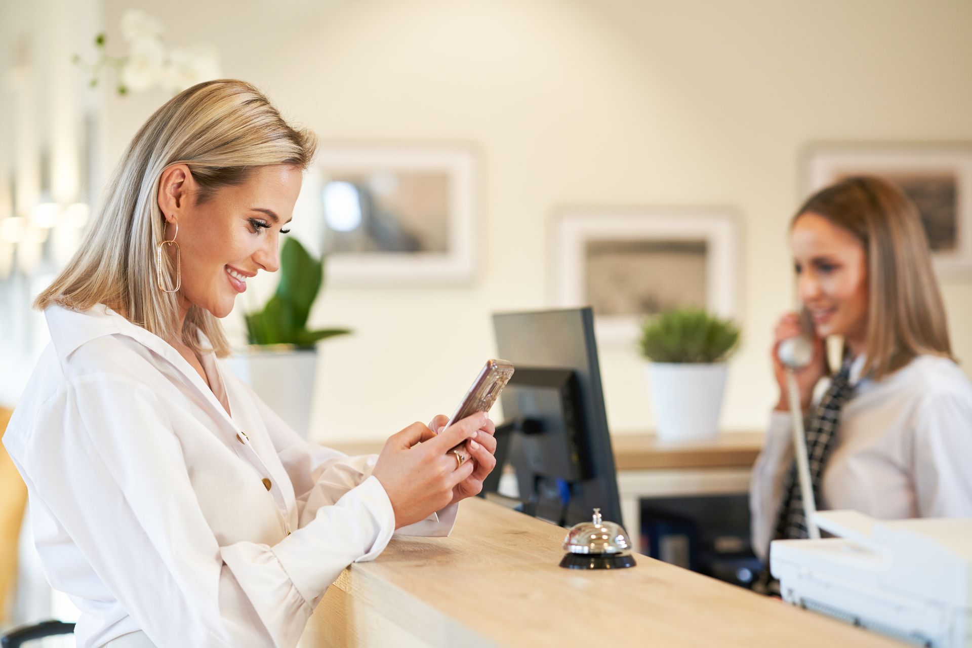 A woman is sitting at a counter in a hotel looking at her cell phone.