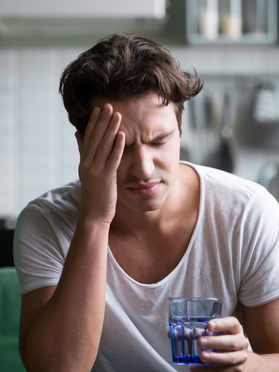A man is holding his head while holding a glass of water.