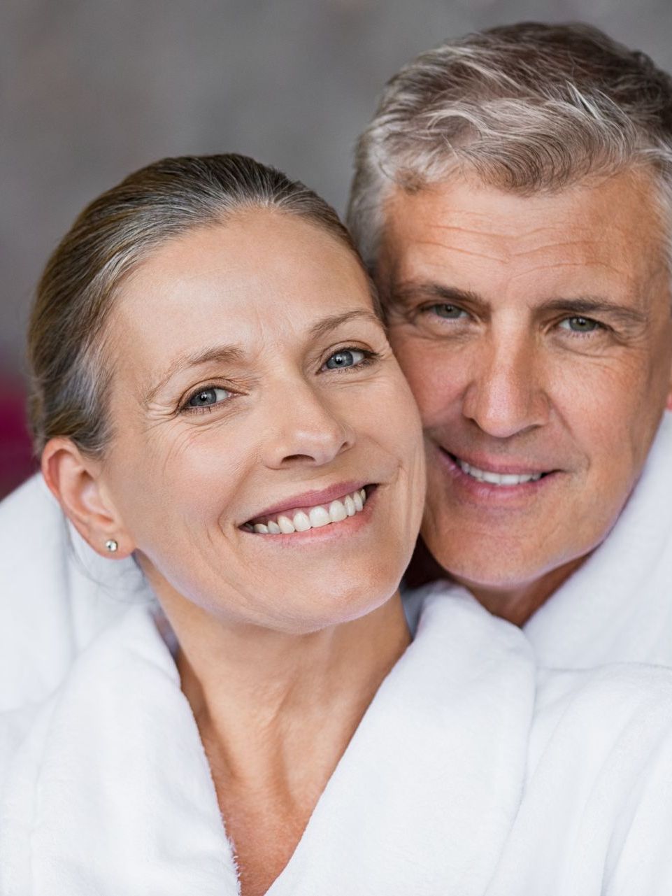 A man and a woman are smiling for the camera while wearing bathrobes.