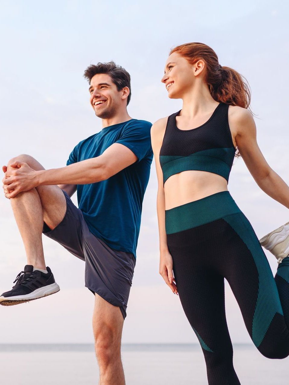 A man and a woman are stretching their legs on the beach.