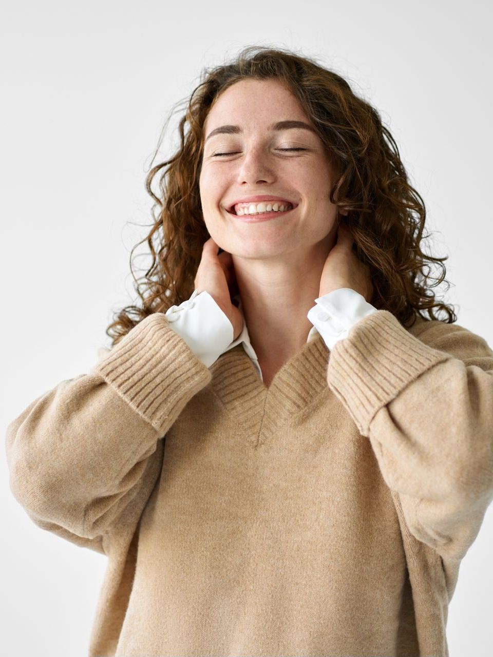 A woman wearing a tan sweater is smiling with her eyes closed.