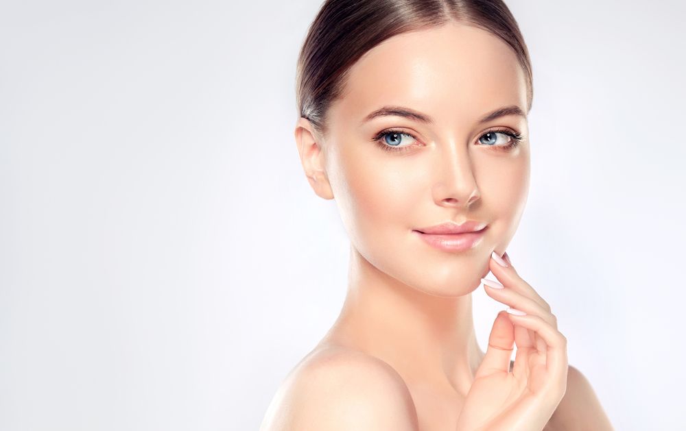 The woman is smiling and touching her face with her hand.
