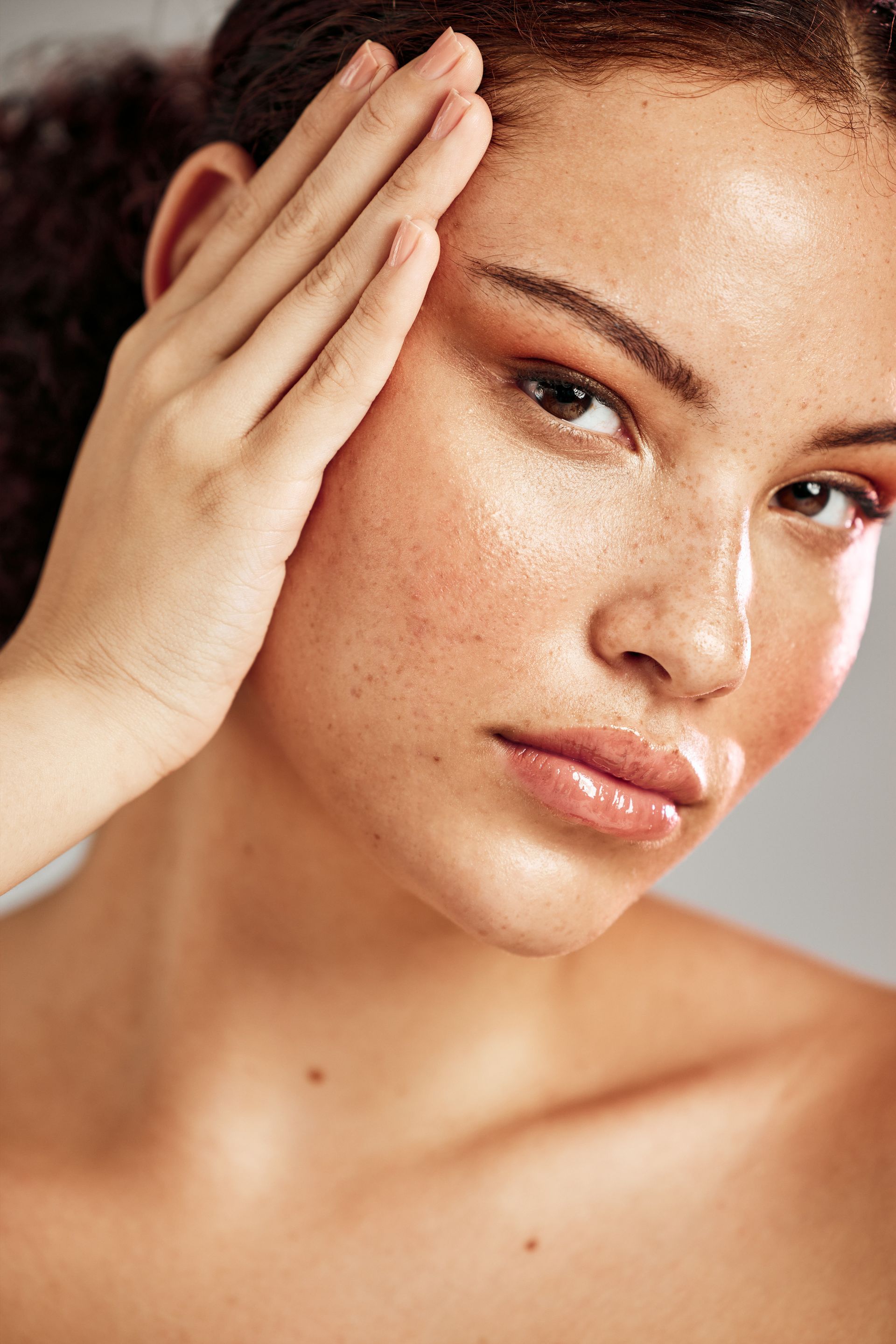A woman is touching her face with her hand and looking at the camera.