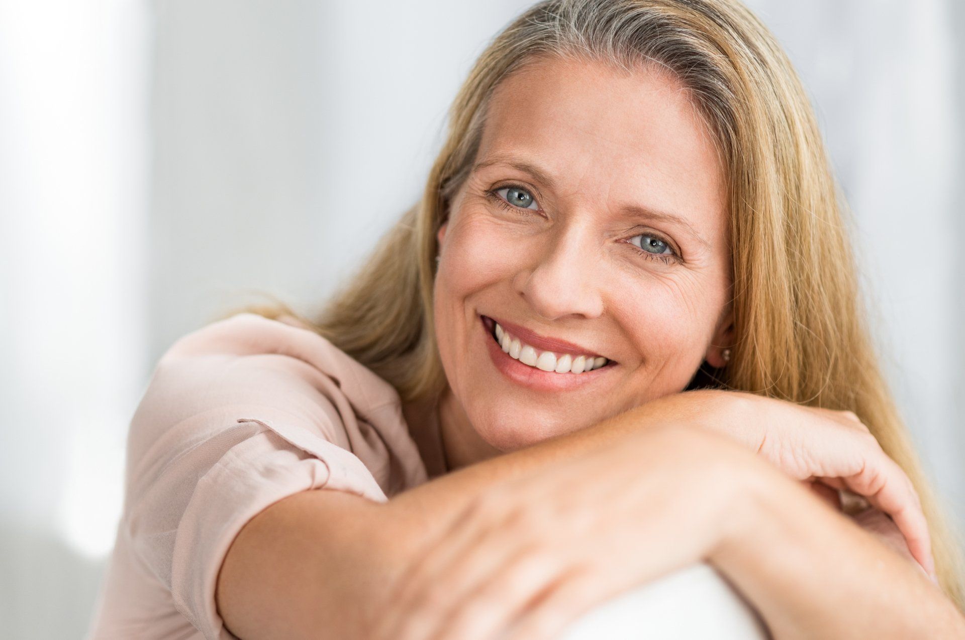 A woman is smiling and hugging her arm while sitting on a couch.