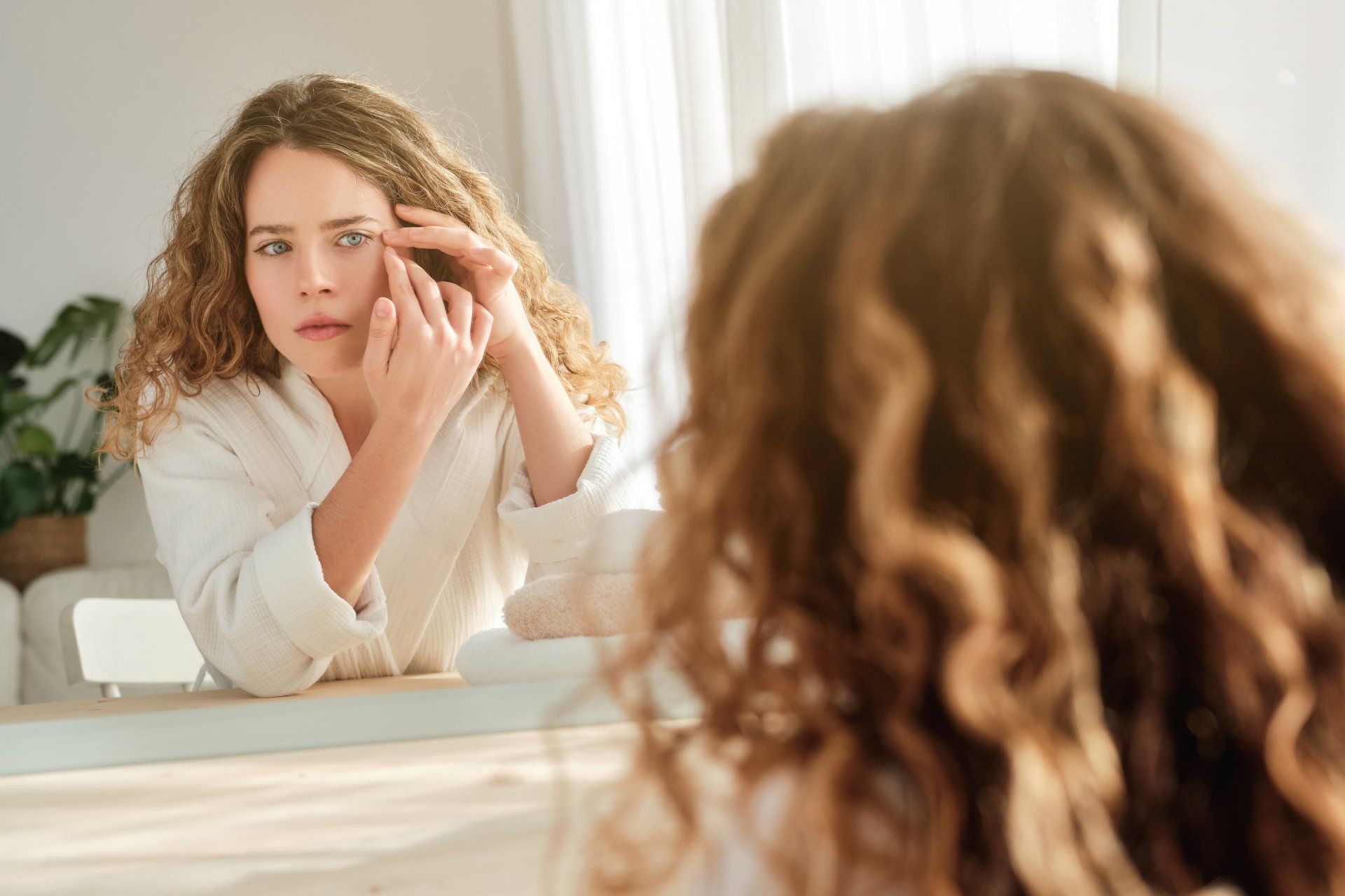 A woman is looking at her face in the mirror.