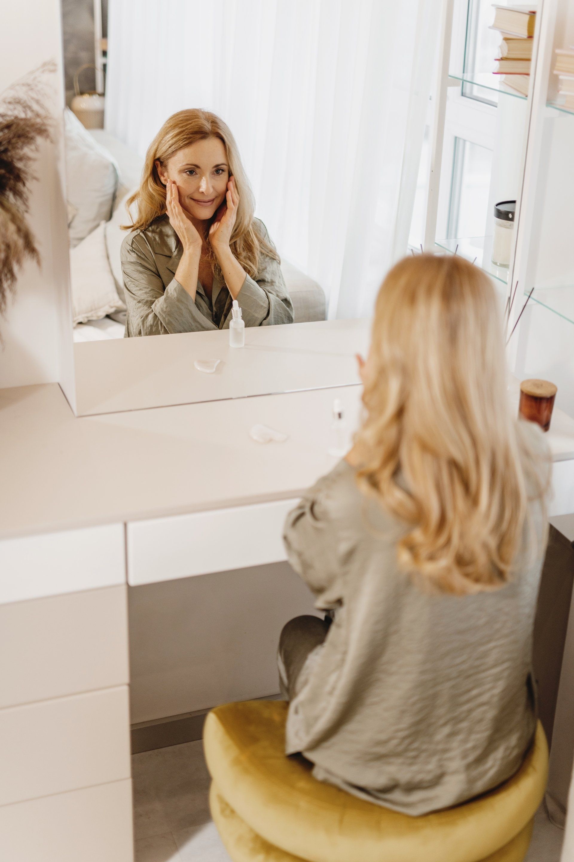 A woman is sitting at a vanity looking at herself in the mirror.