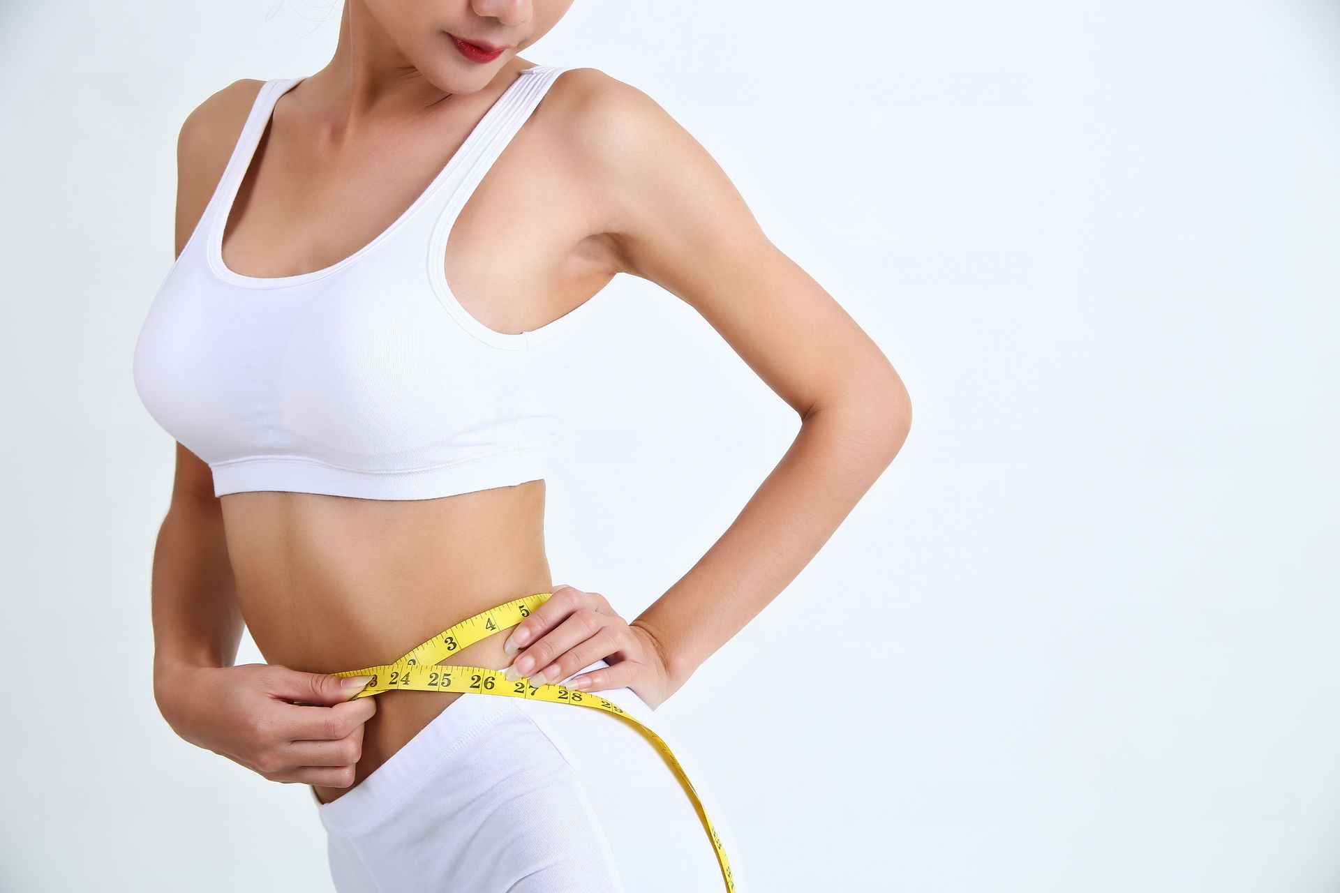A woman is measuring her waist with a tape measure.
