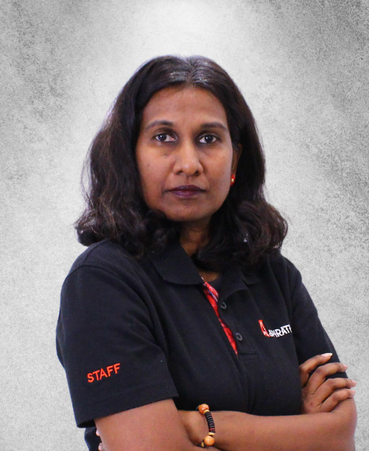 A person with dark hair and a serious expression, wearing a black staff polo shirt with arms crossed against a grey background.