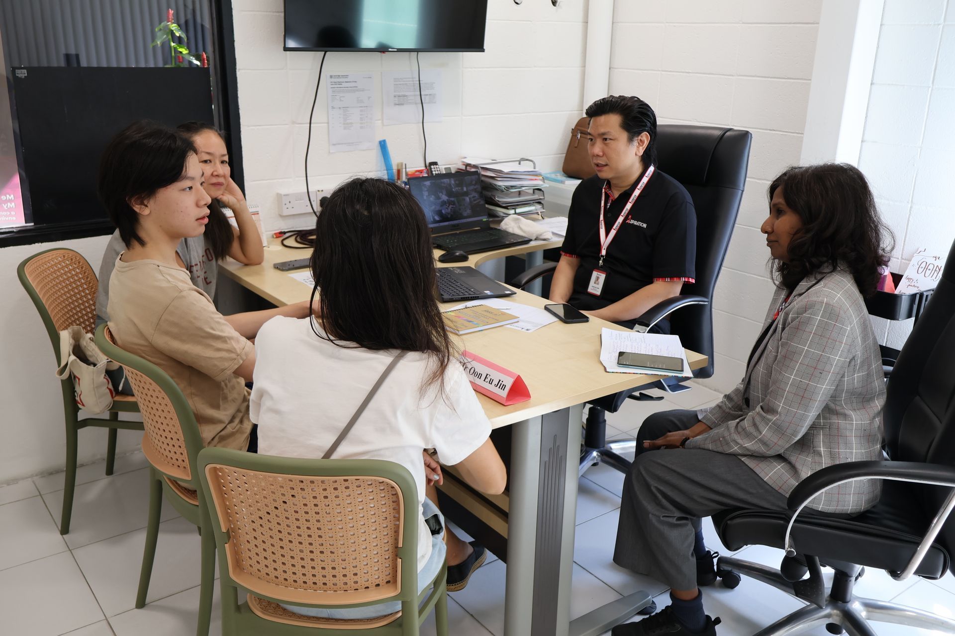 A diverse group of people sitting around a desk in an office, engaging in a discussion.