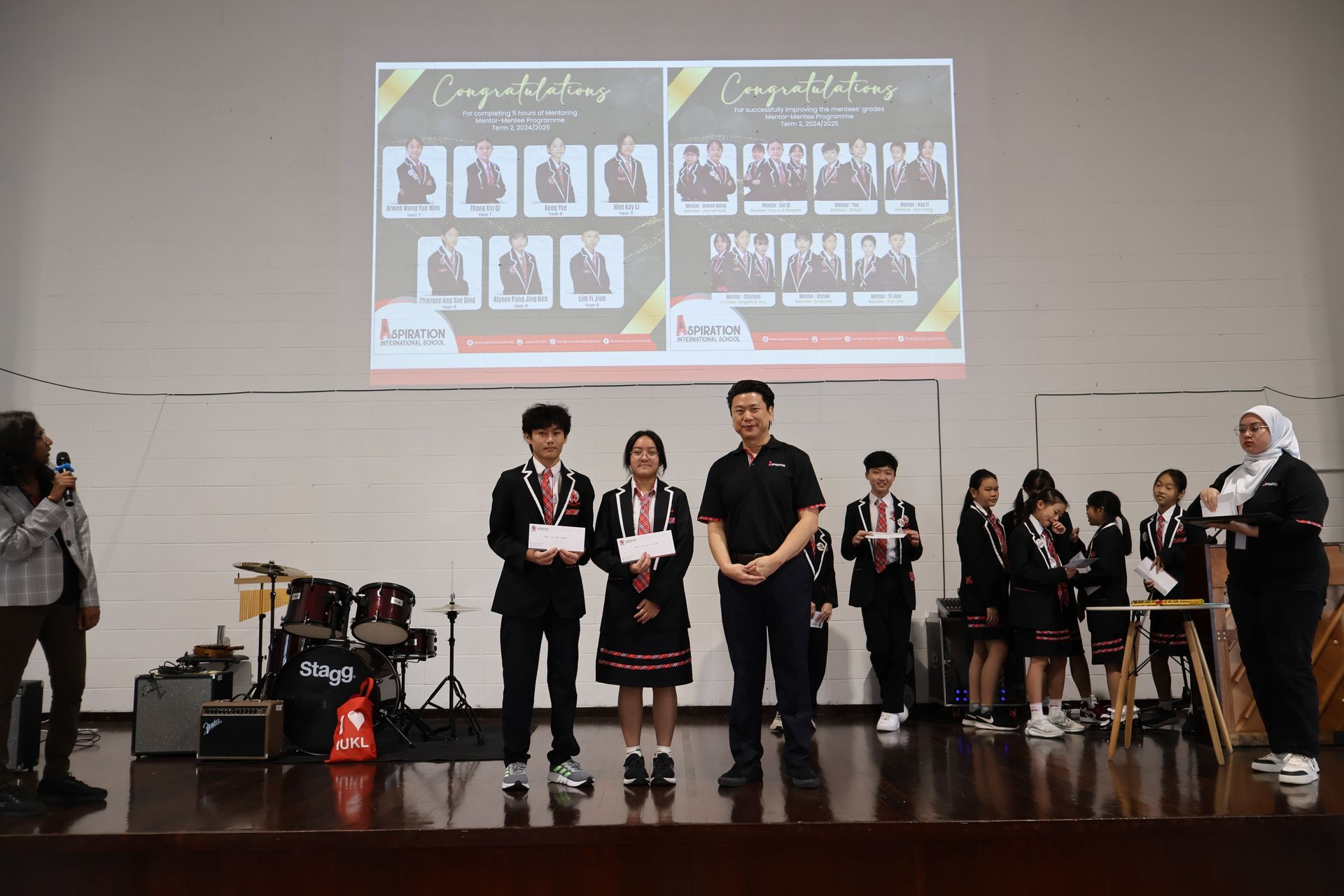 A group of students on stage receiving awards, with a congratulatory presentation slide projected behind them.