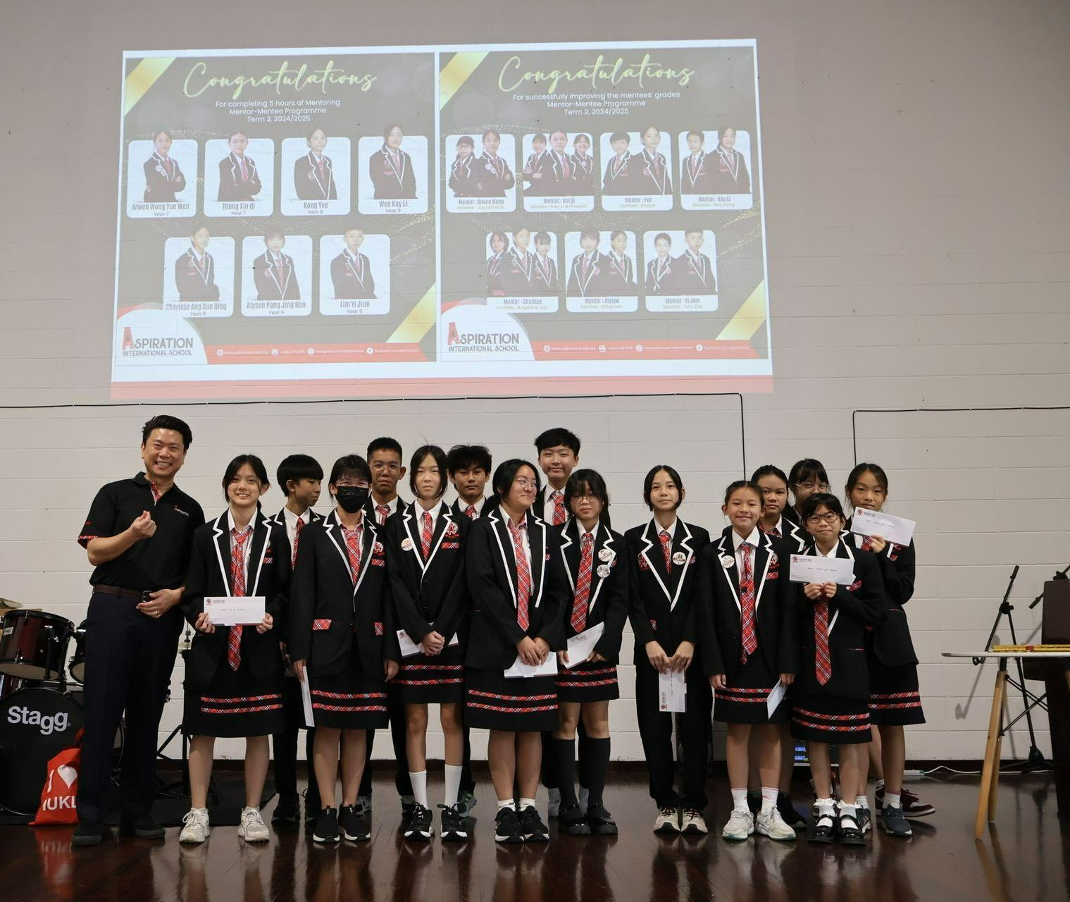 A group of students in matching school uniforms standing on stage during an awards ceremony with a digital presentation.