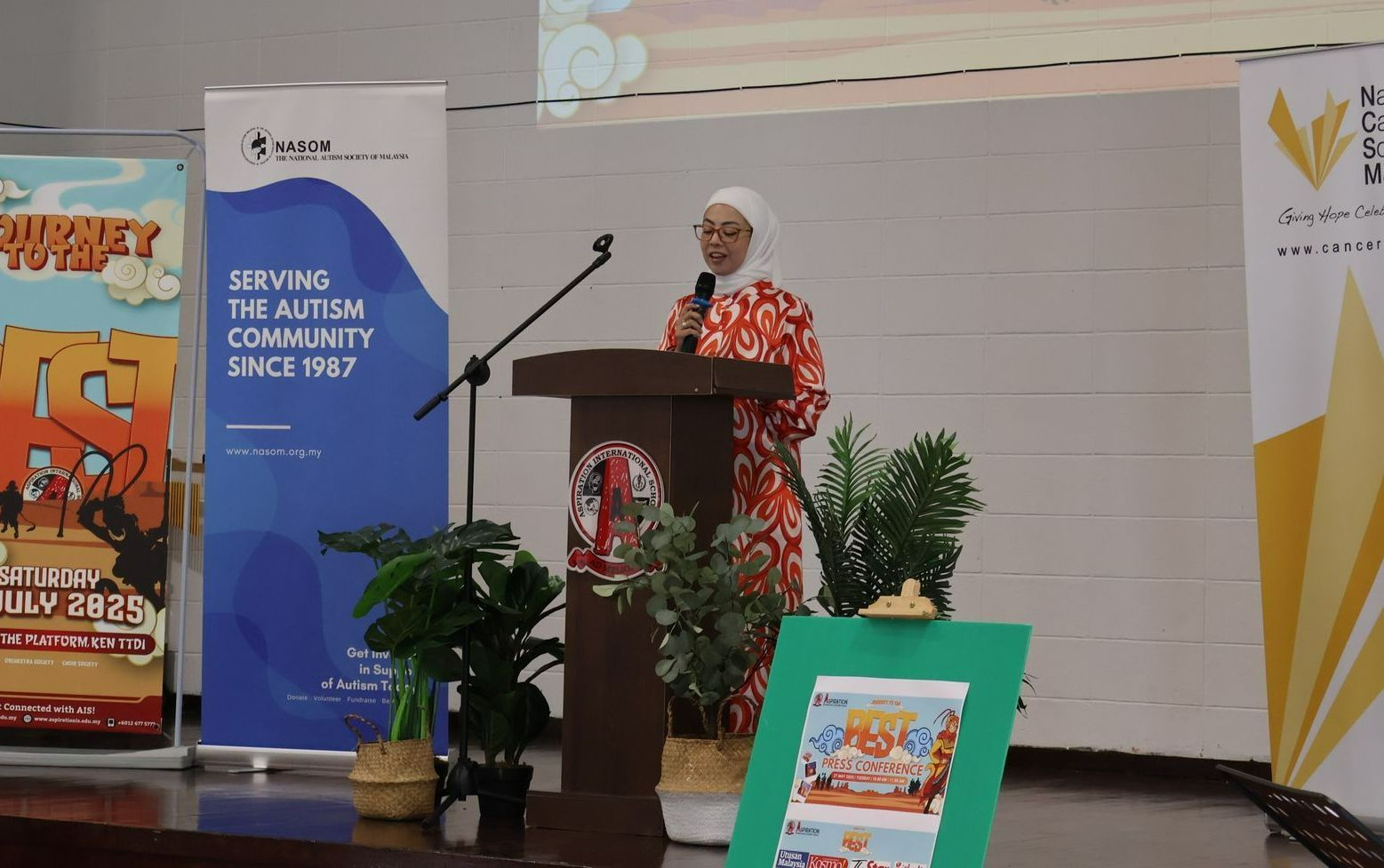 A person in a patterned dress speaks at a podium during an event with autism advocacy banners in the background.