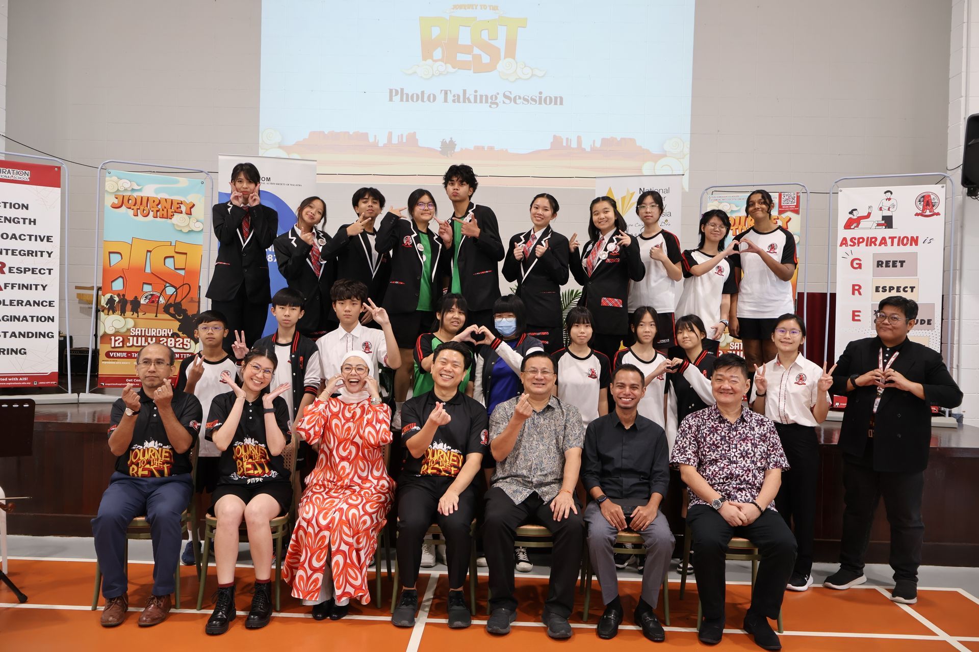 A group of students and staff pose for a photo at a school event with a banner reading 