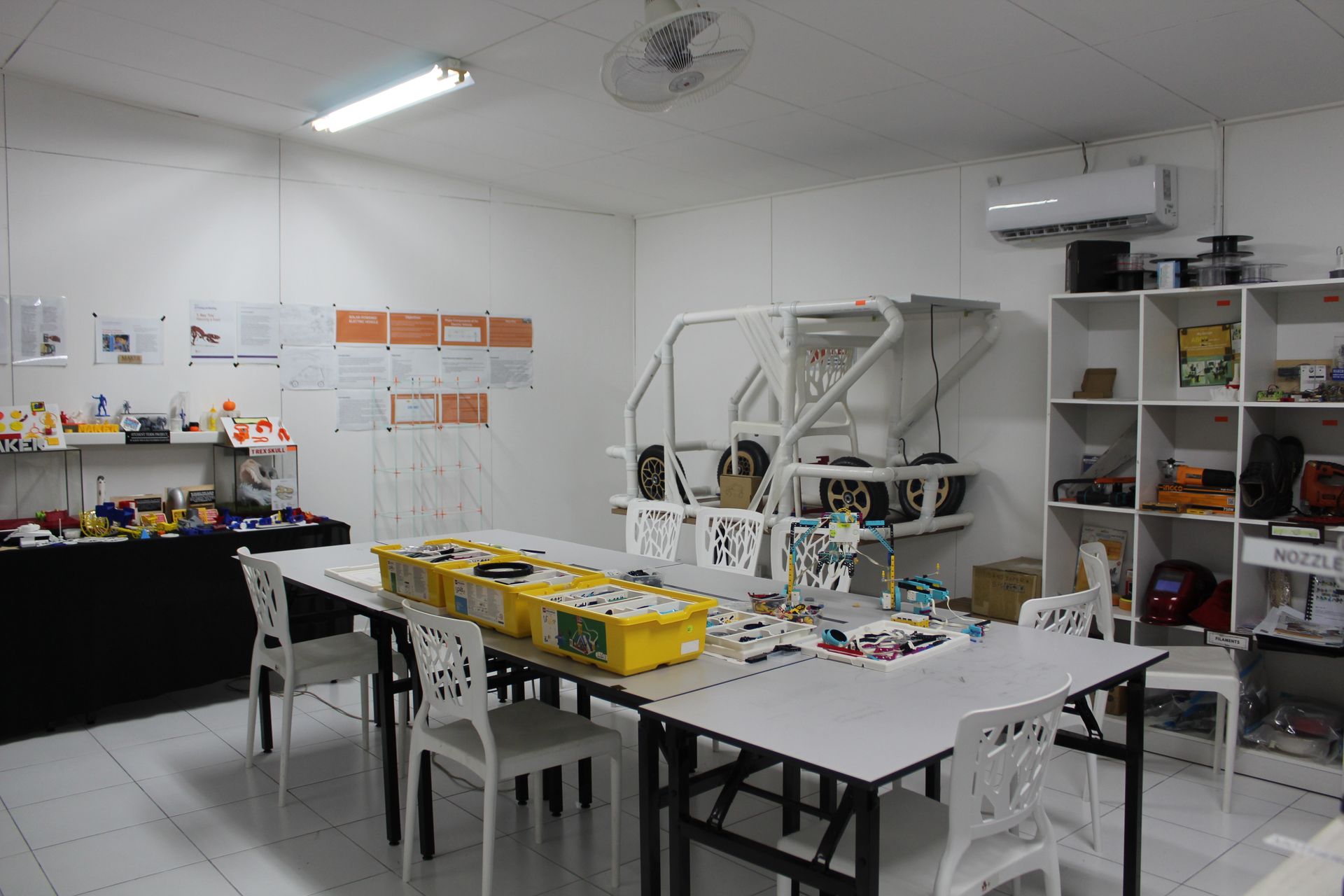 A white-walled room with a workbench featuring modular yellow storage bins, a metal frame structure, and shelving units.