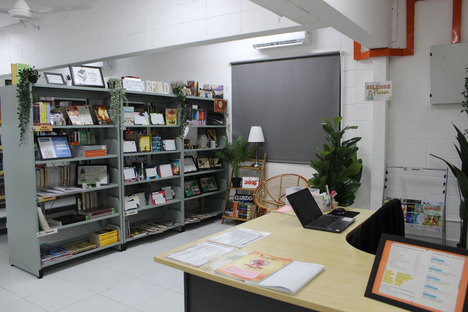 A desk with a laptop faces shelves of books in a brightly lit, modern office or library setting.