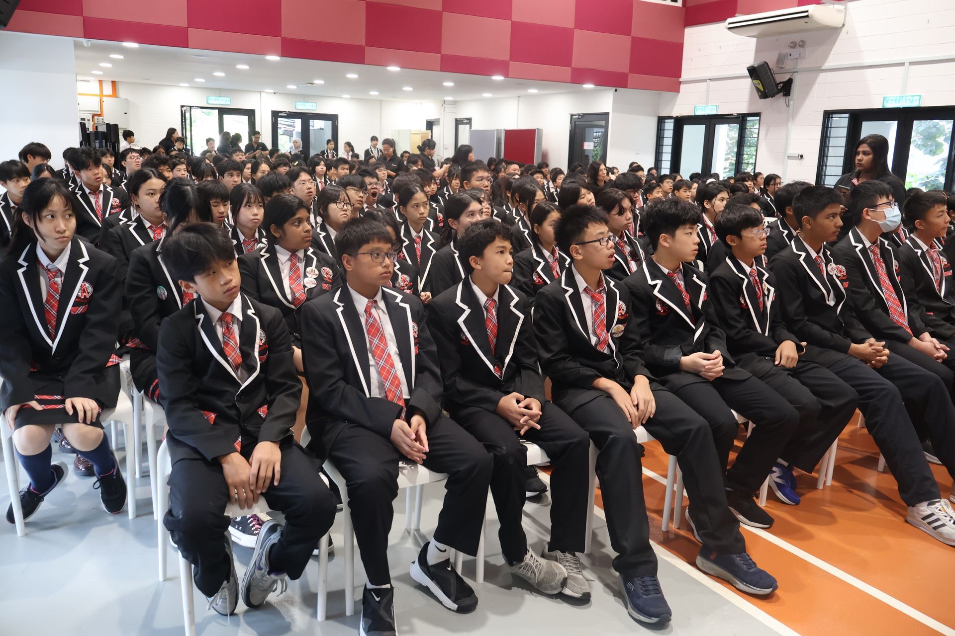 A large group of students in school uniforms sitting together and listening attentively during a school event or presentation.