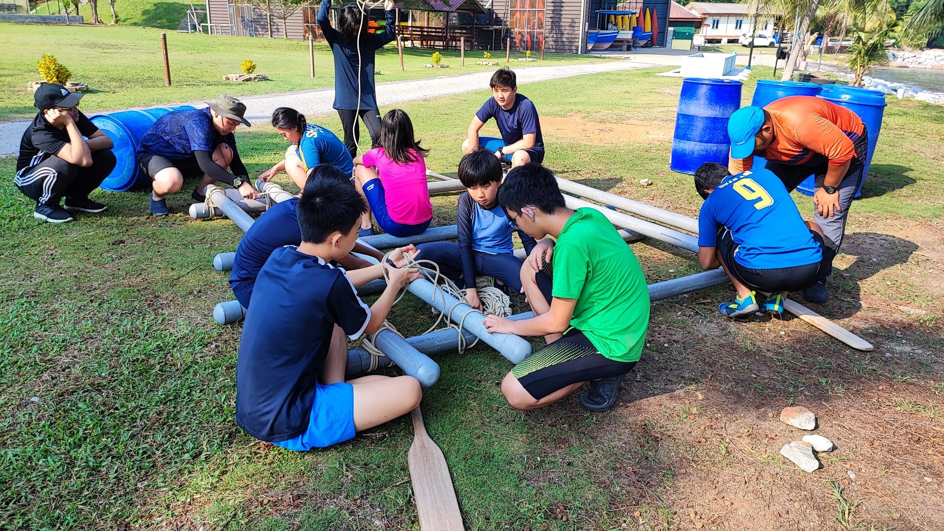 A group of people working together to construct a raft out of pipes and wooden planks in an outdoor field.
