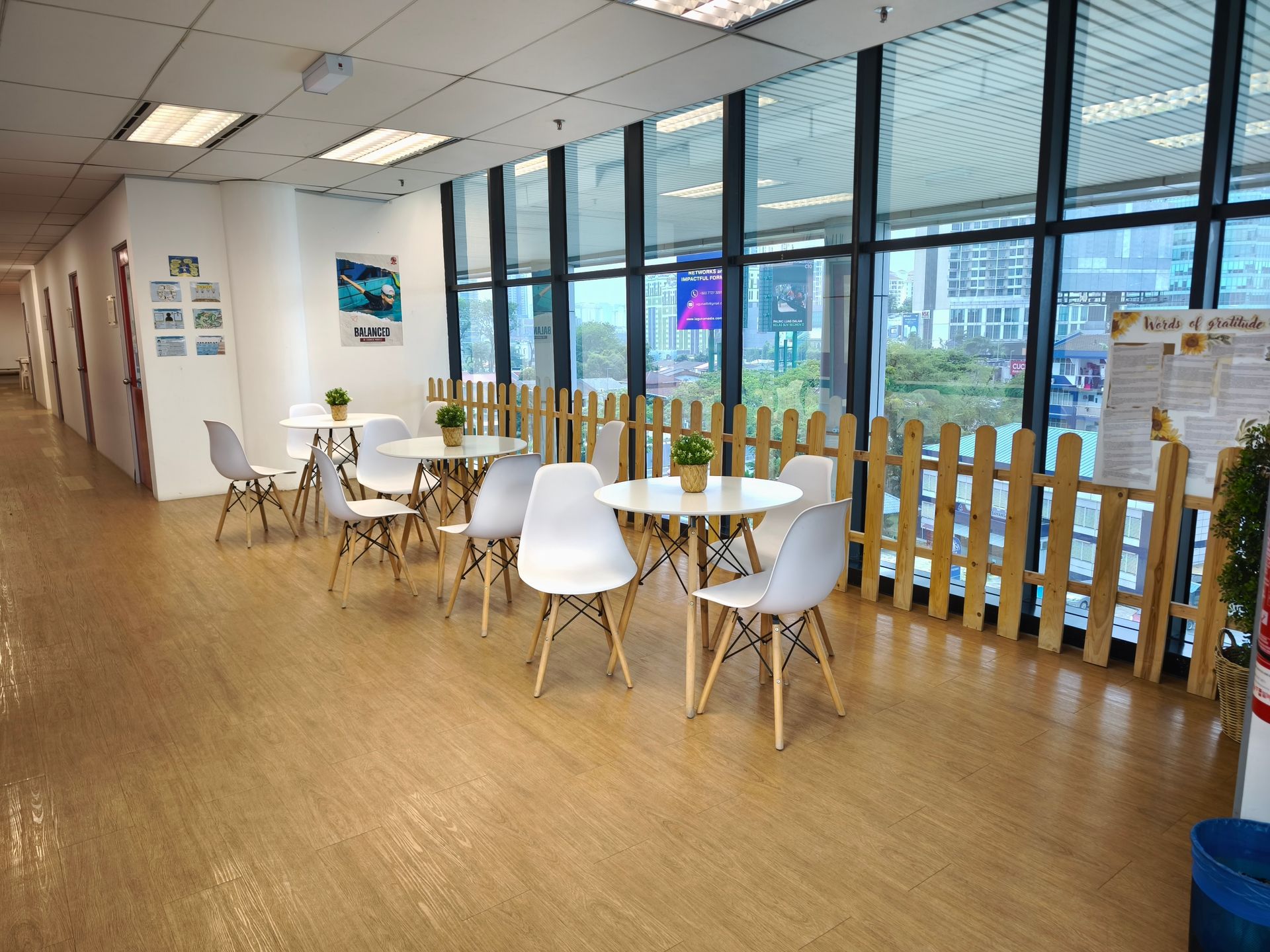 A modern office lounge with white Eames-style chairs and small circular tables placed by a large window.