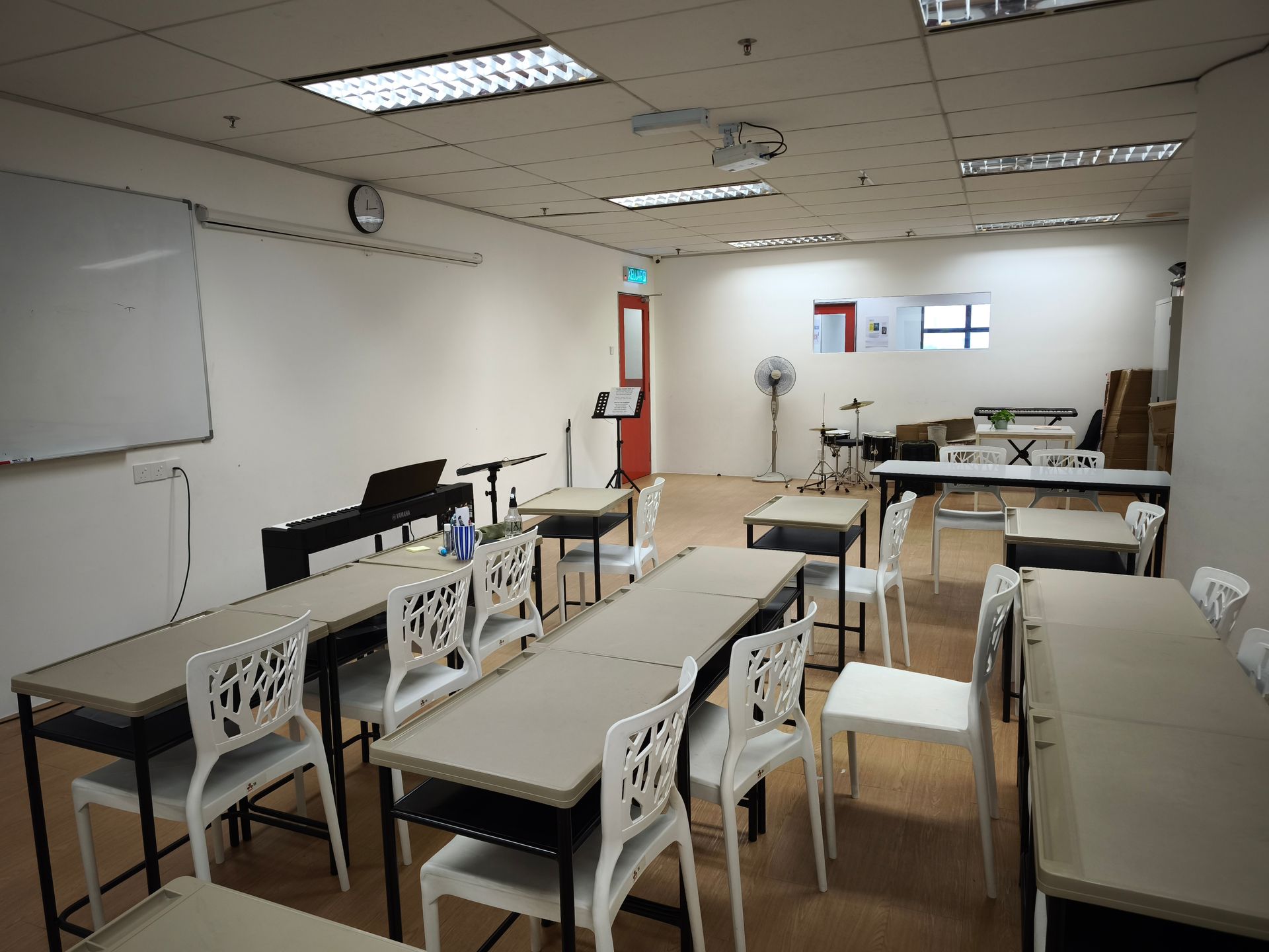 A classroom with tables, white chairs, and musical instruments including a keyboard and drums in the background.