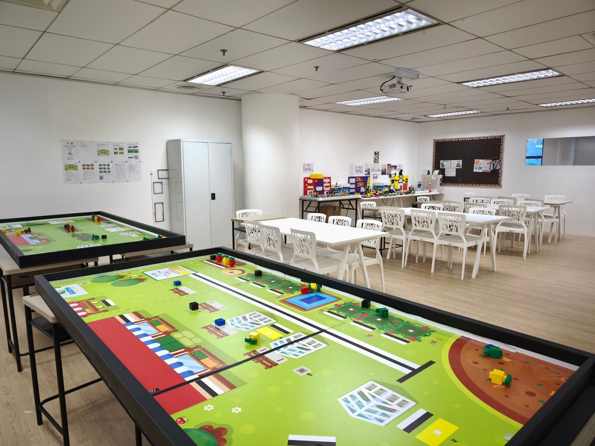Activity room with two large game tables, white chairs, and cabinets in a bright, modern indoor space.