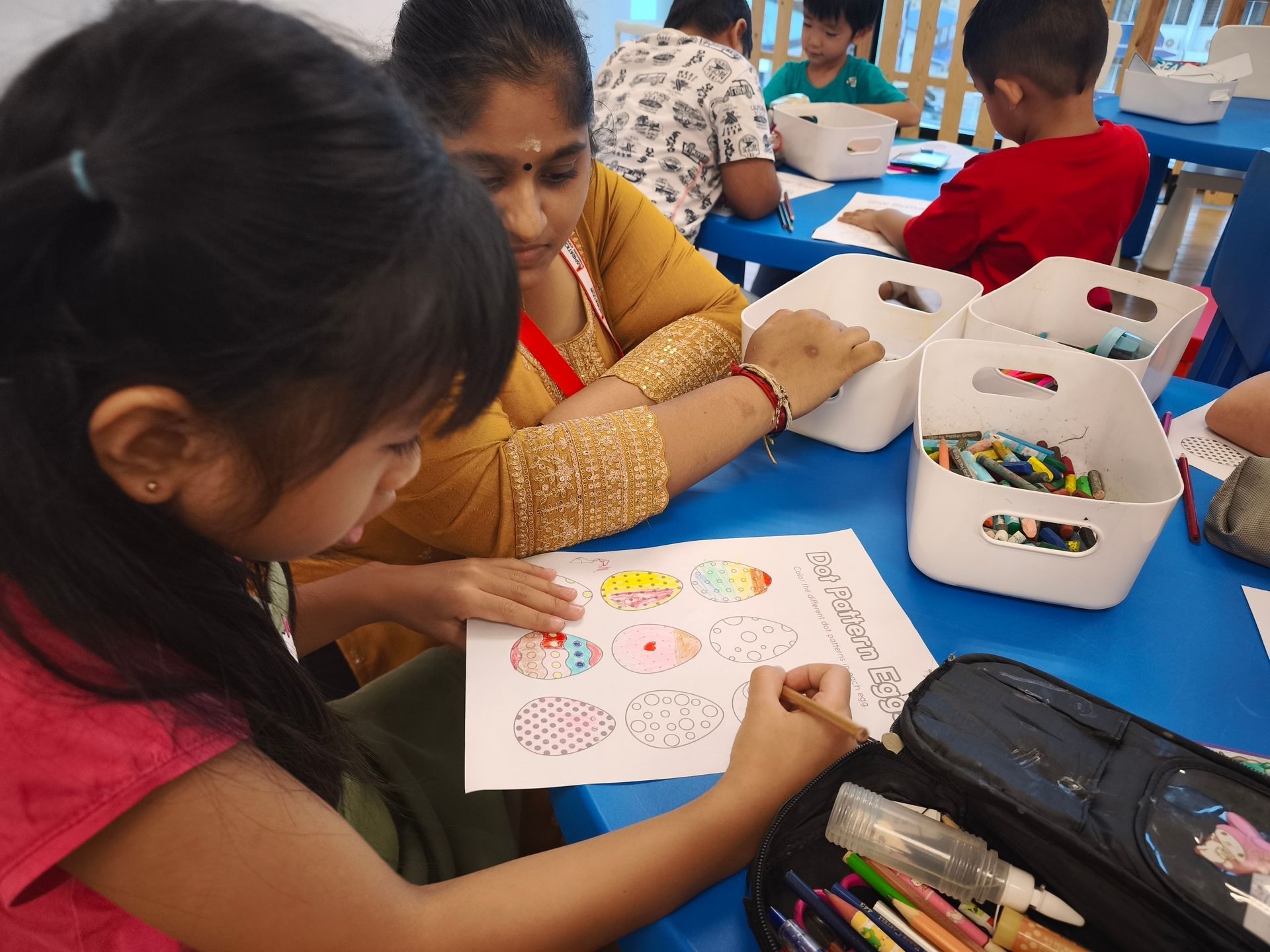 A child and an adult sitting at a blue table, working together on a worksheet with colorful drawings of Easter eggs.