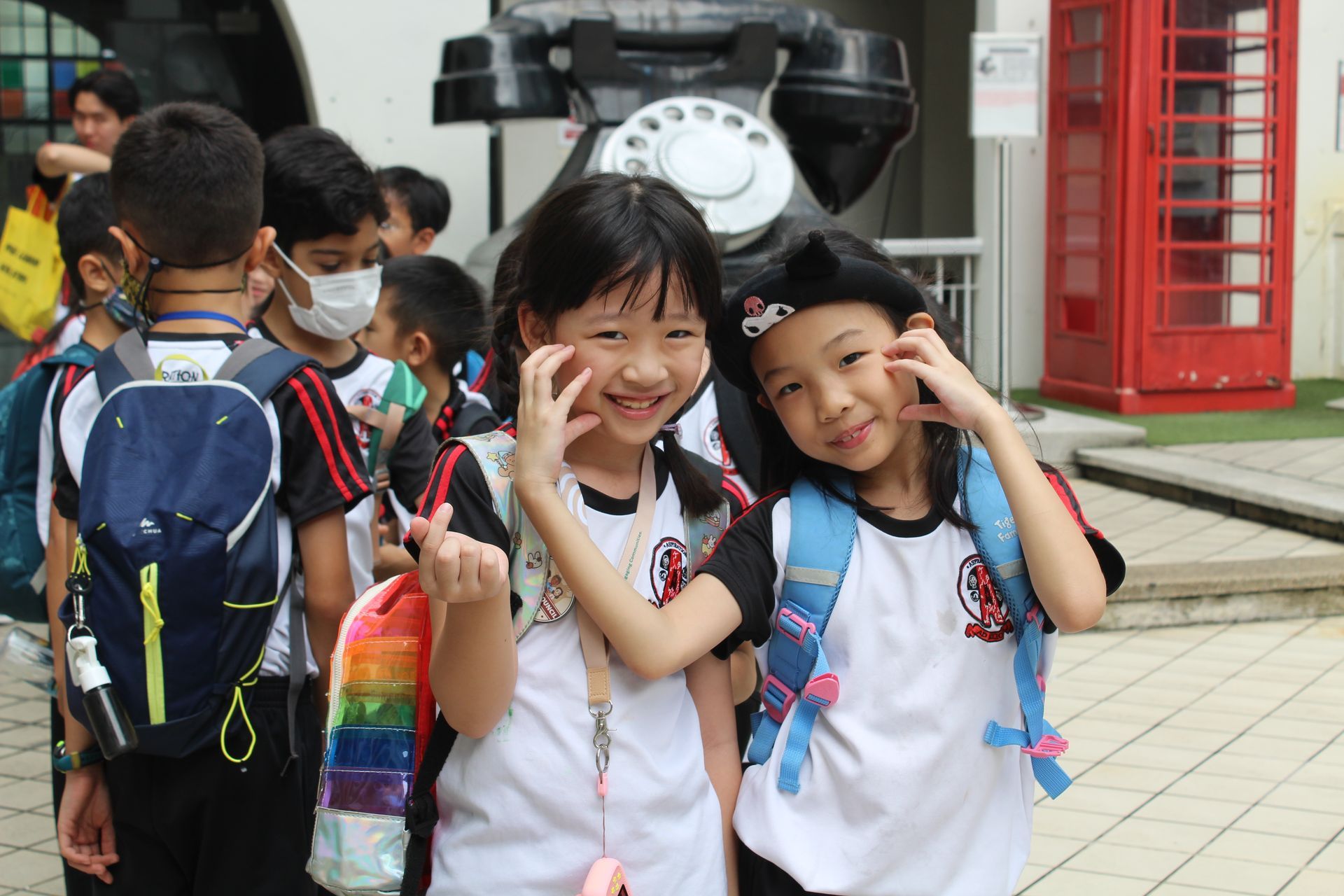 Two children smiling and posing in front of a giant telephone sculpture and a red telephone booth.