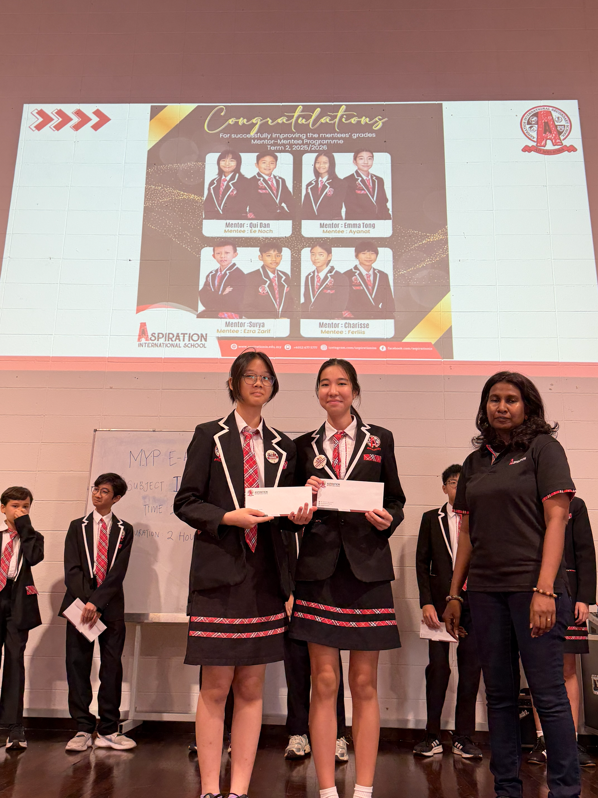 The students receive certificates or awards alongside their teacher, celebrating their hard work.