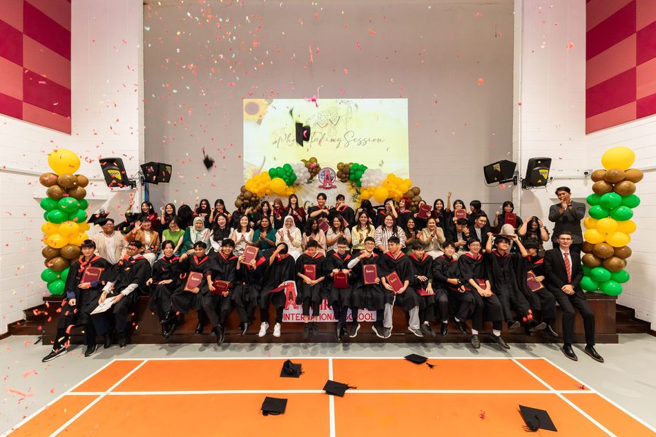 Graduates in academic regalia toss caps into the air at a ceremony, cheering and holding diplomas in an indoor hall.