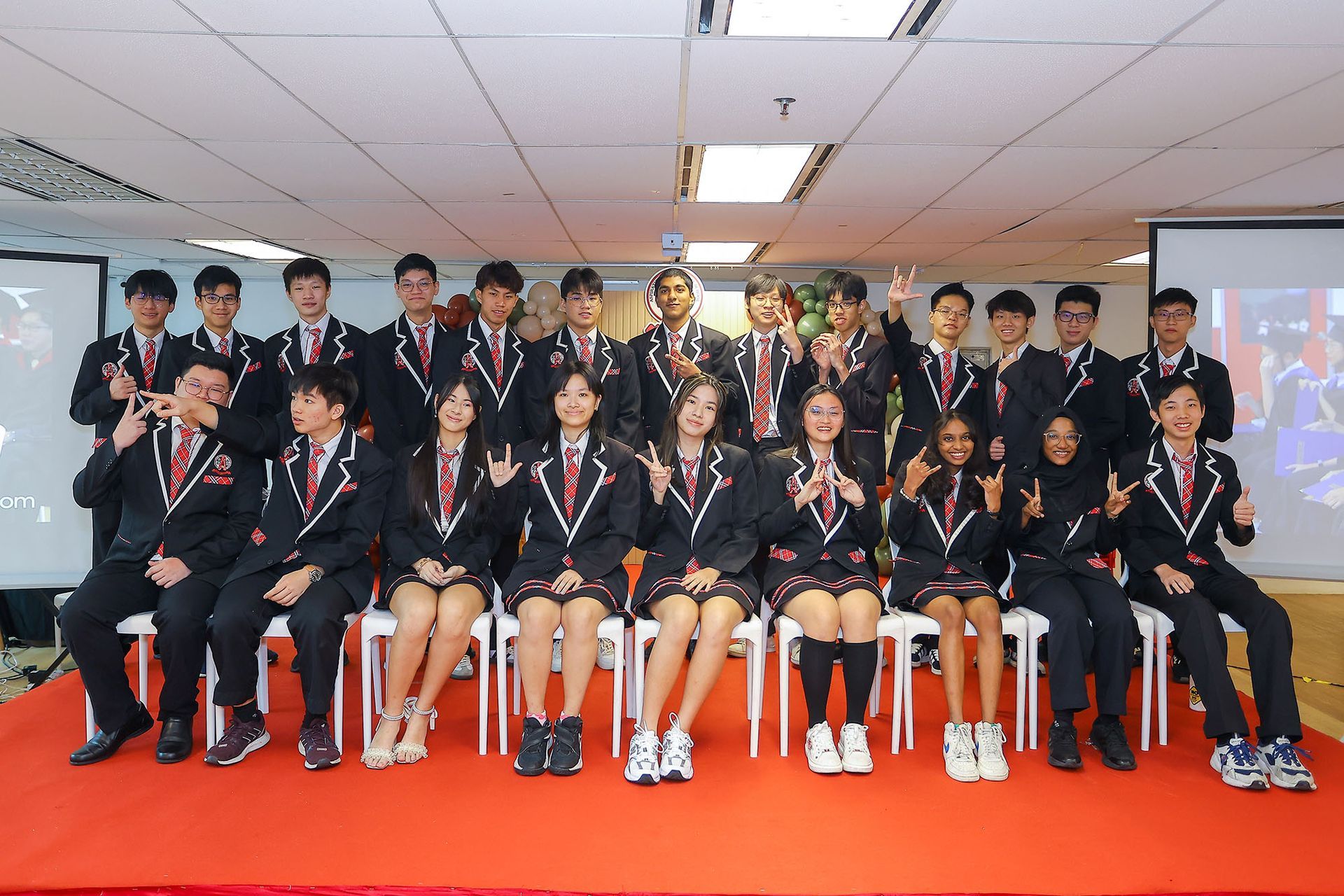 A group of people wearing matching blazers and ties pose for a formal portrait on a stage with a red carpet.