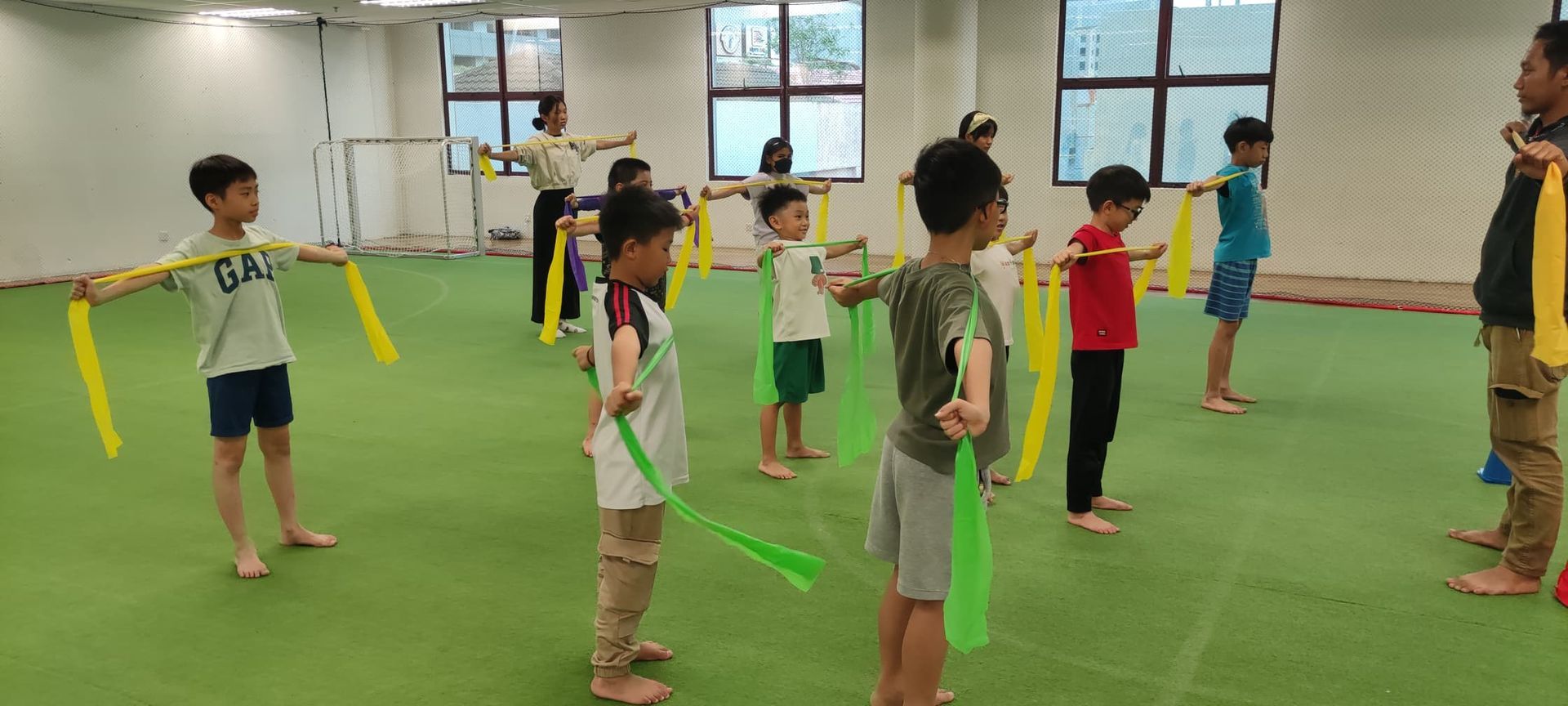 A group of children and instructors in a gym holding resistance bands while standing in lines during an exercise class.