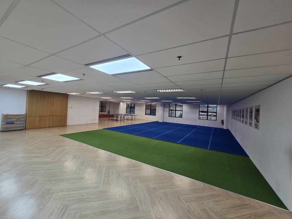 An indoor space with a herringbone wood floor, a green turf area, and a blue workout mat, featuring recessed lighting.