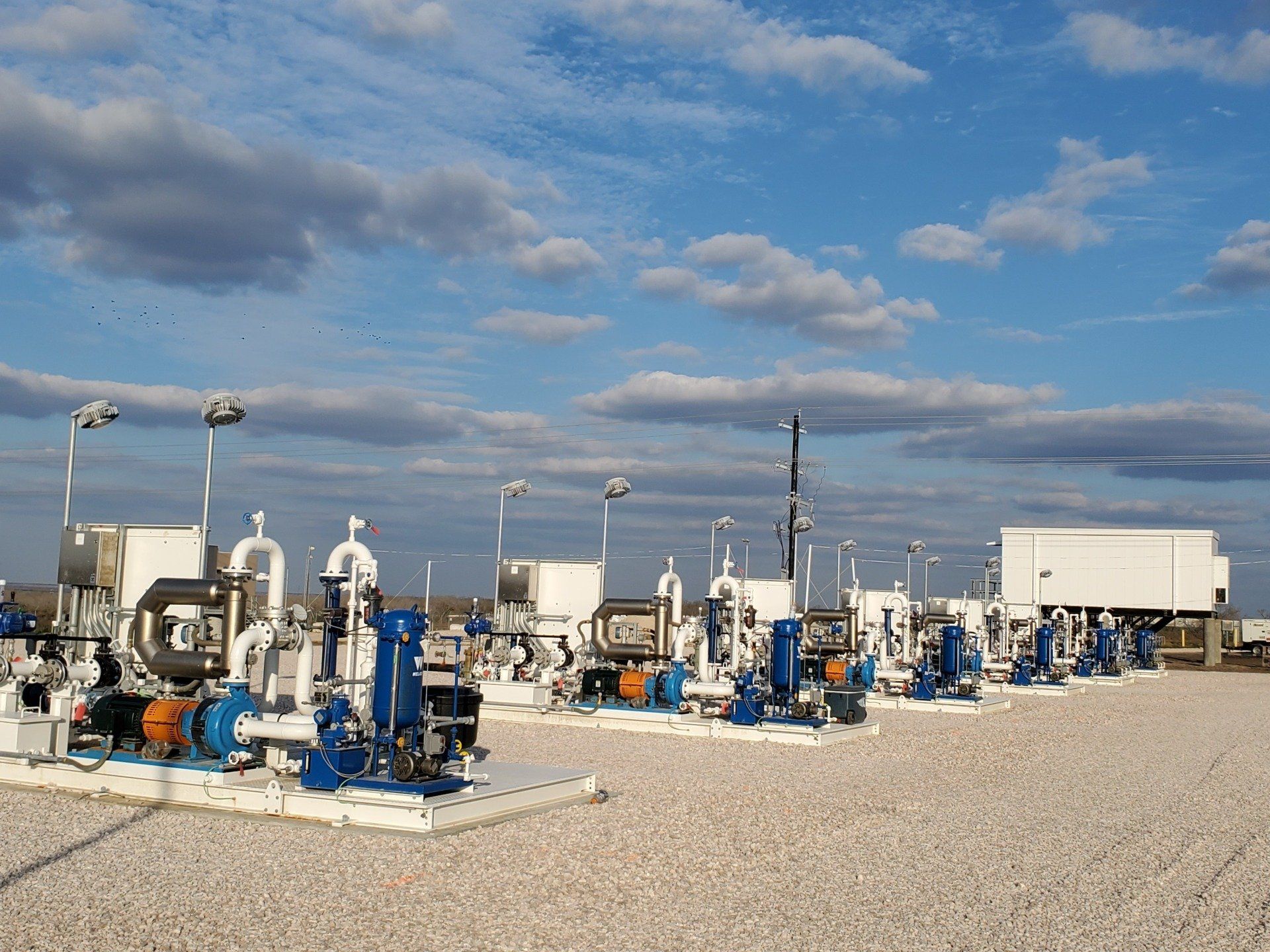 Industrial oil and gas equipment on a gravel site under a blue, partly cloudy sky