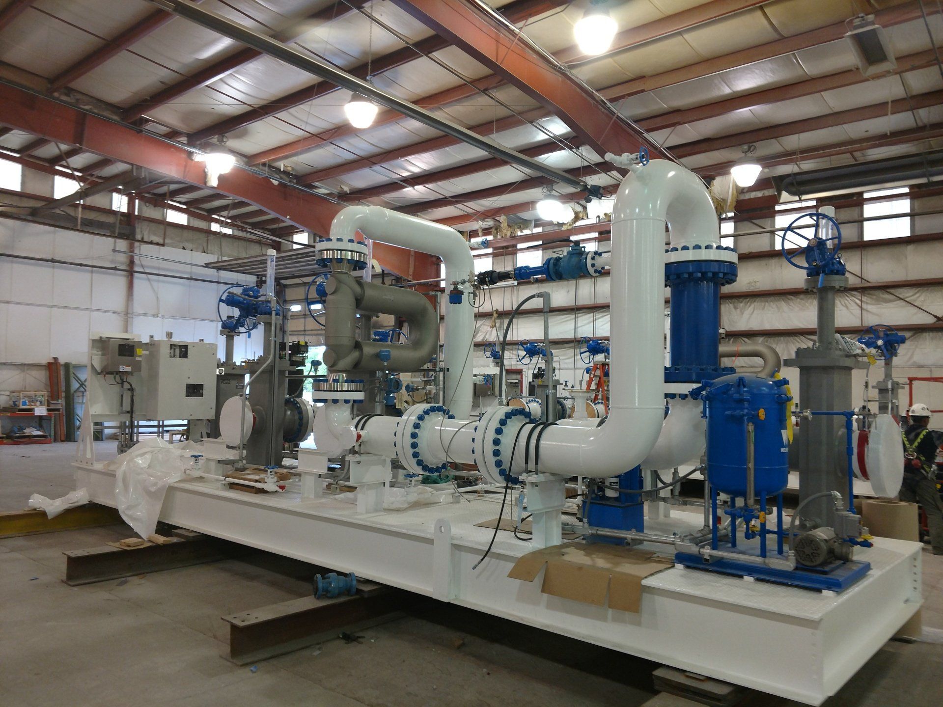 Industrial machinery with large white pipes and blue pumps inside a warehouse facility