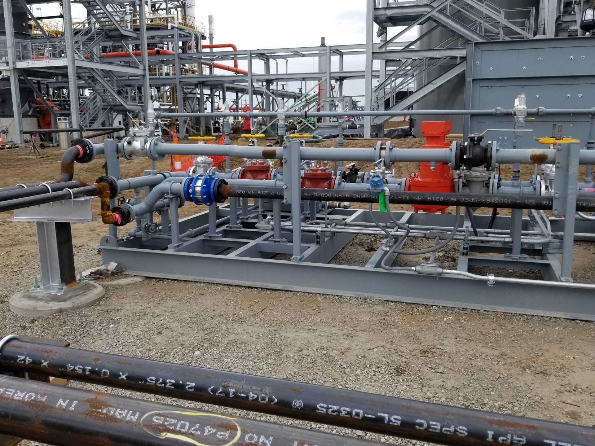 Industrial pipeline equipment with red valves and blue pumps in a refinery setting